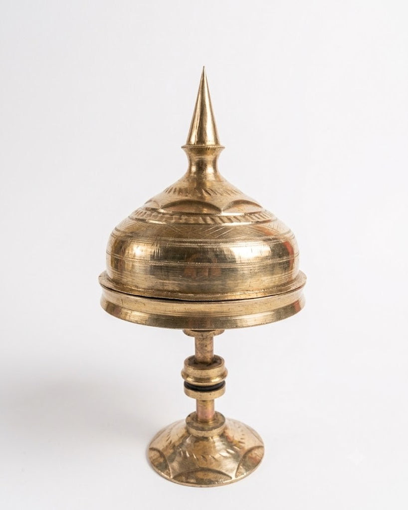 The xorai with its lid on, against white: a spired lid on a domed cover over the tray, a turned stem with collars and a flared foot, all in burnished brass.