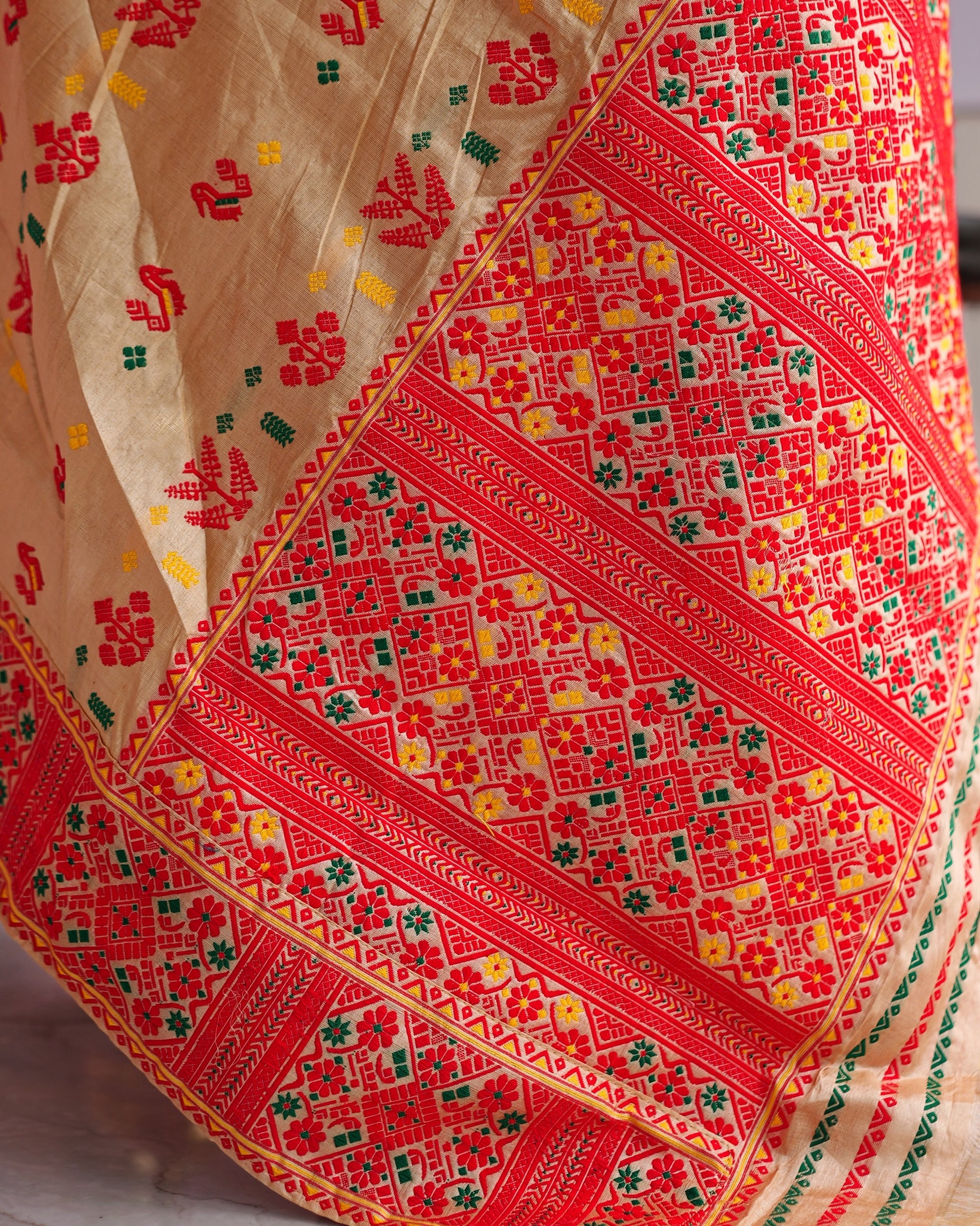 A corner of the drape close up. Red birds, red trees and small green and yellow marks on the beige ground, beside wide red bands of diamonds and rosettes edged with fine yellow lines.