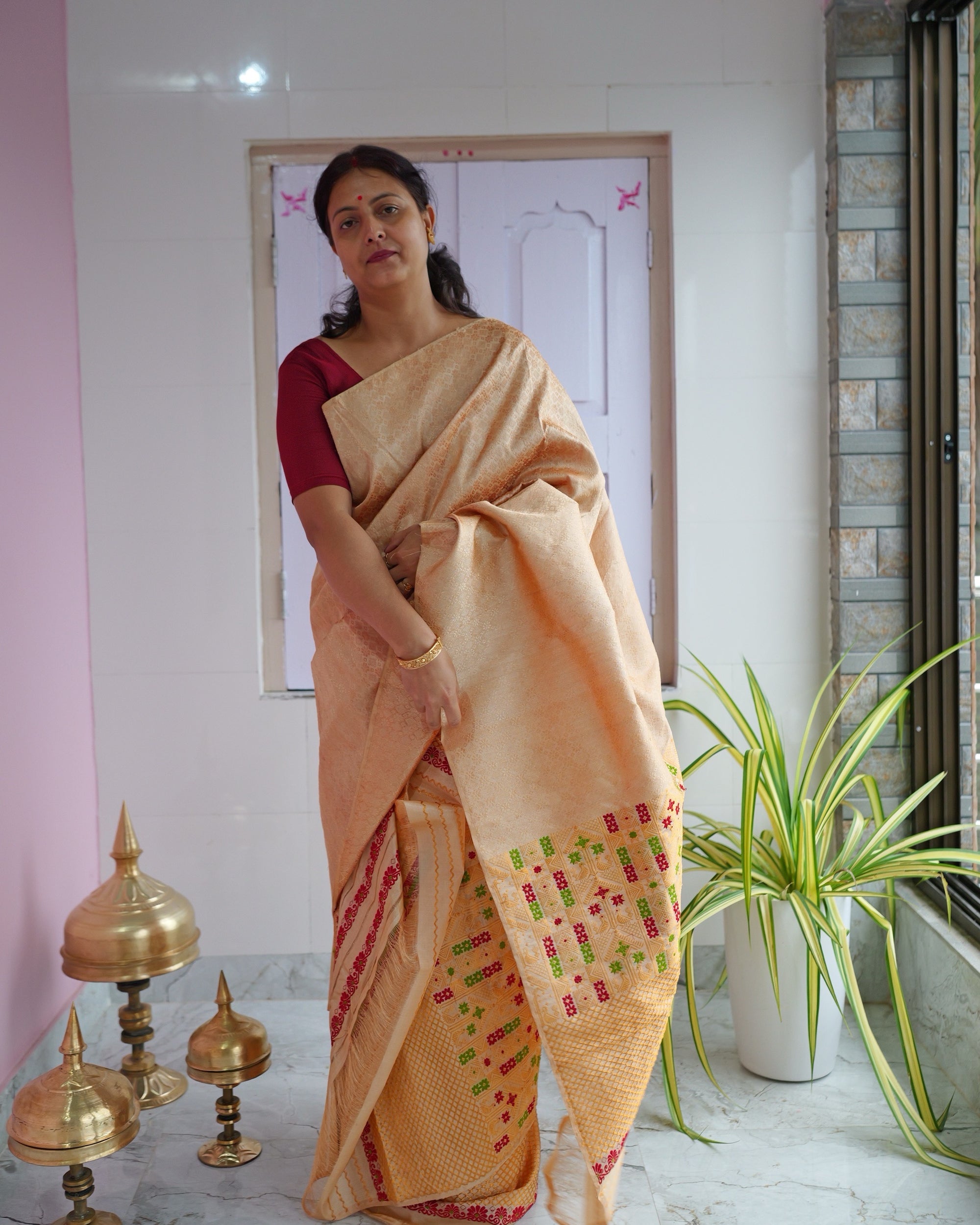 Standing on a verandah with a pink wall and three brass xorai on the floor, the set seen full length.