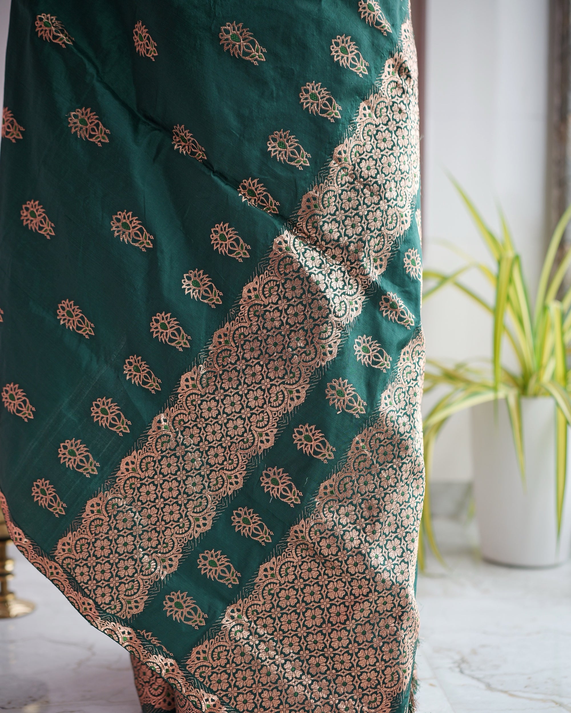 The drape folded diagonally. A wide band of rose-gold rosette lattice running across the emerald ground between rows of floral buti.