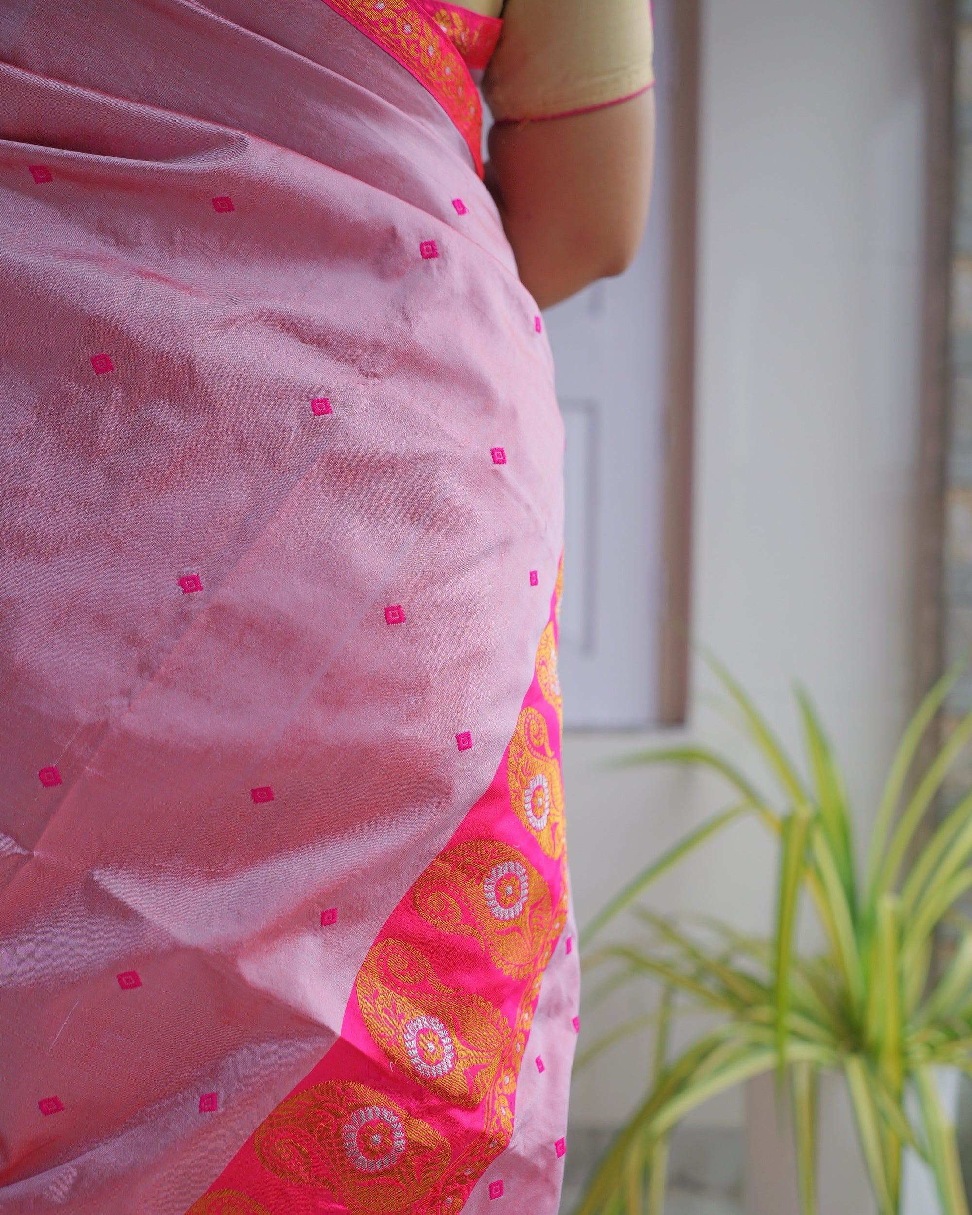 The rose-pink drape close up, scattered with small magenta square buti, over the magenta mekhela and its band of zari rosettes.