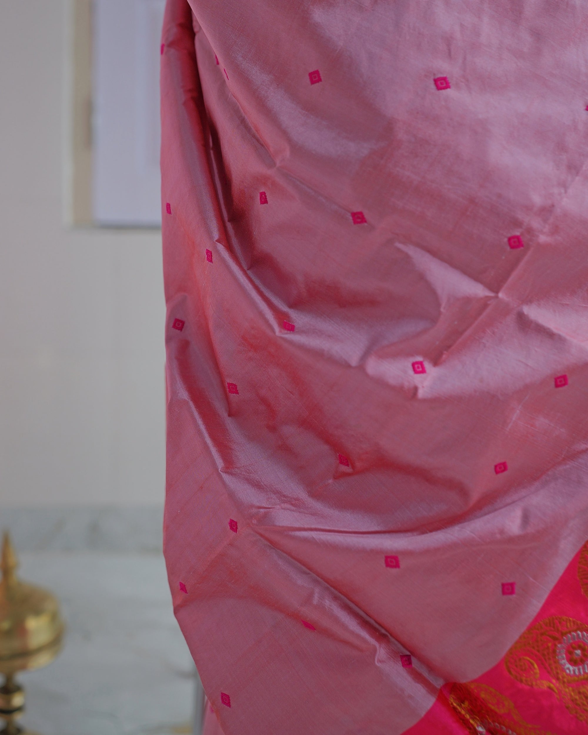 The rose-pink sador hanging in folds, small magenta square buti across a surface that shifts between pink and lilac.