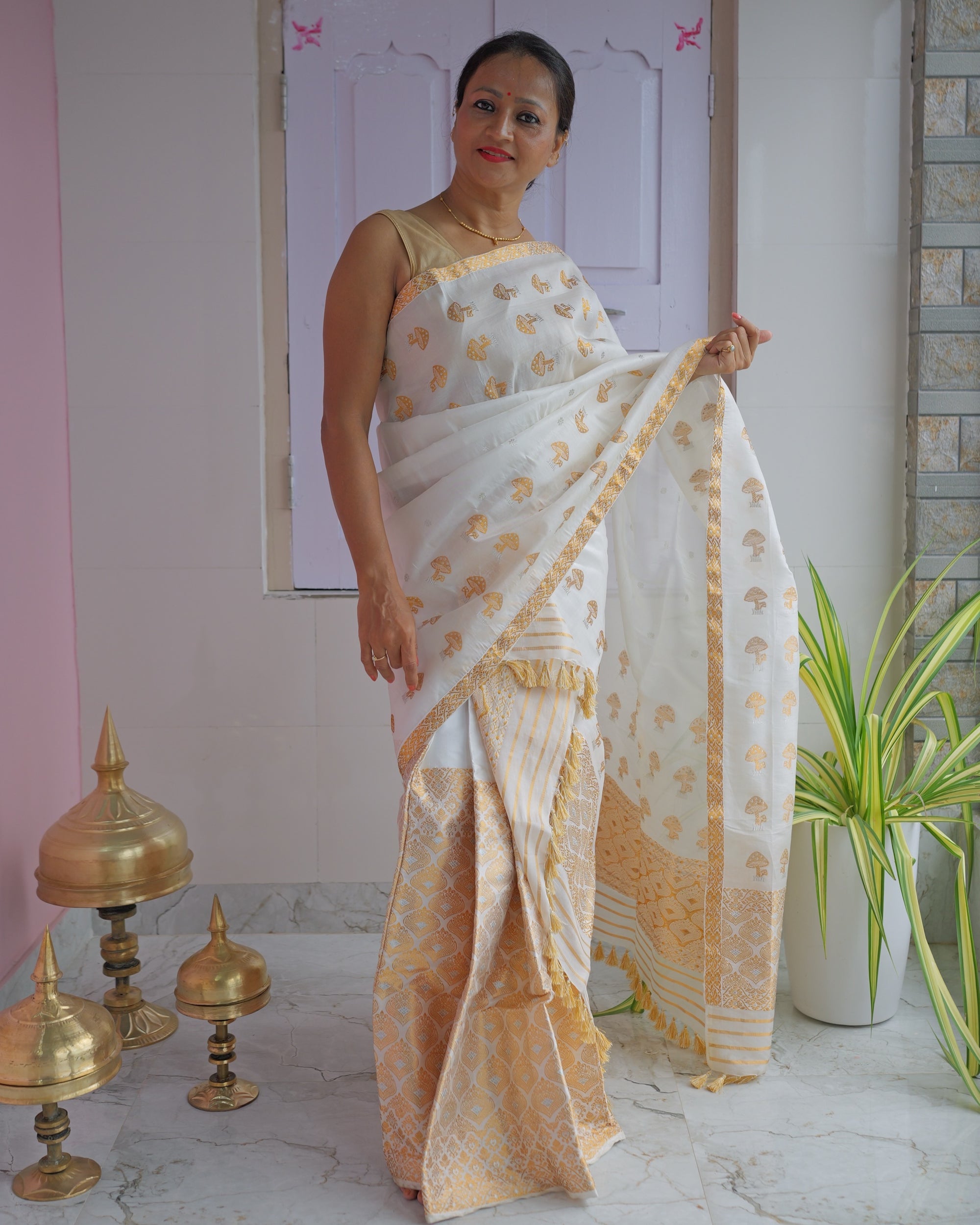 Standing on a verandah with a pink wall and brass xorai on the floor, the set seen full length.