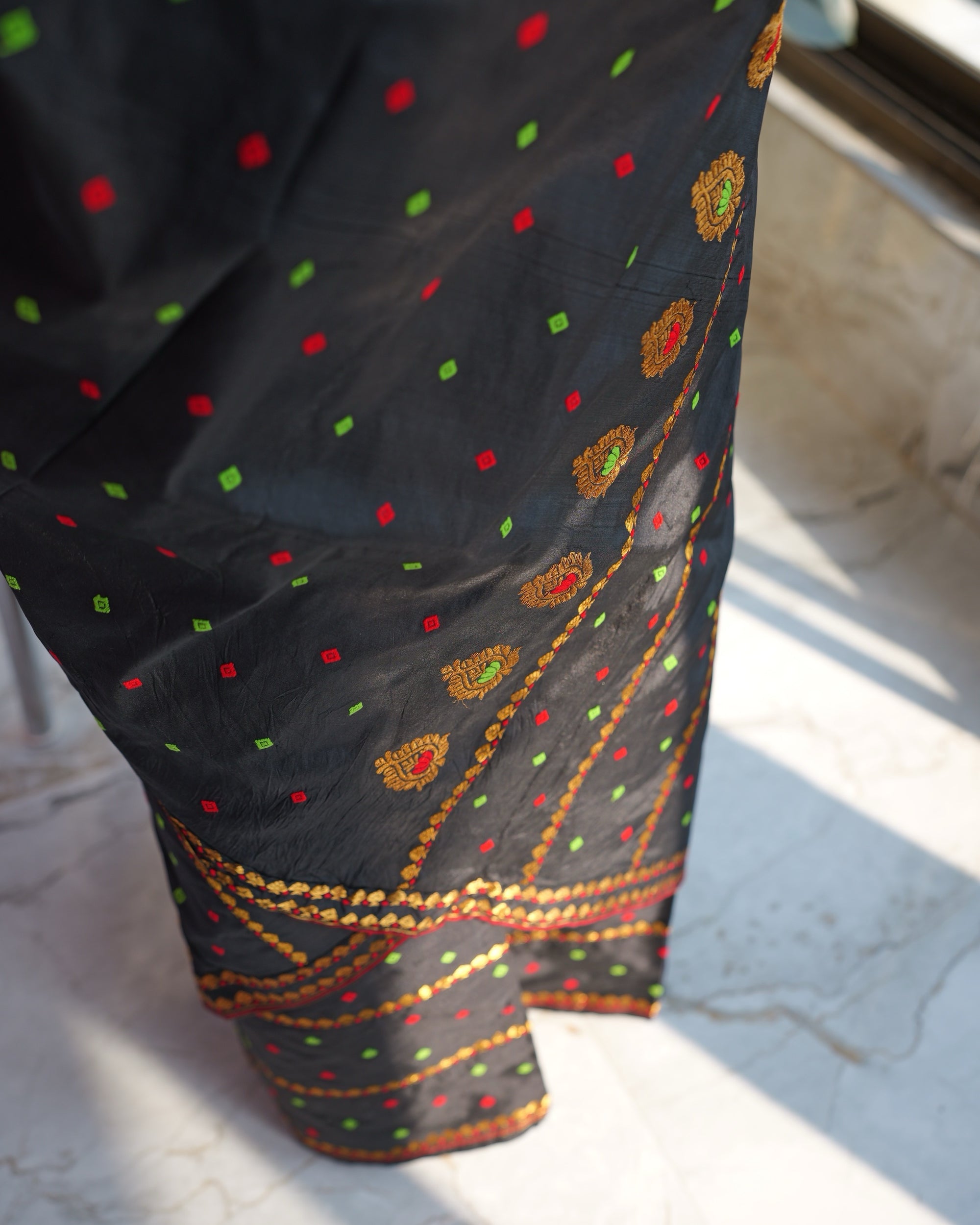 Looking down the black drape: red and green squares, and a line of round gold flowers whose hearts alternate red and green, running down to gold bands at the hem.
