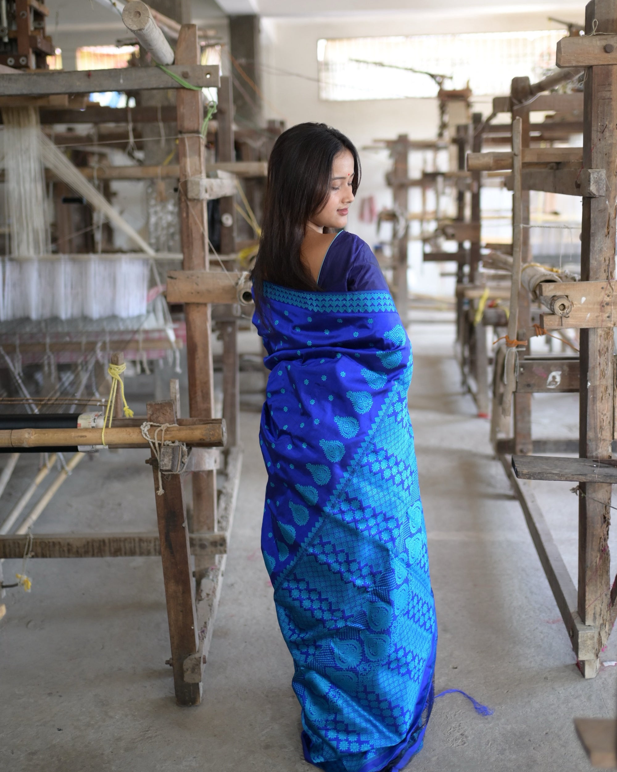From behind with the head turned aside: the pallu hanging down the back, worked in turquoise from the shoulder to the hem.