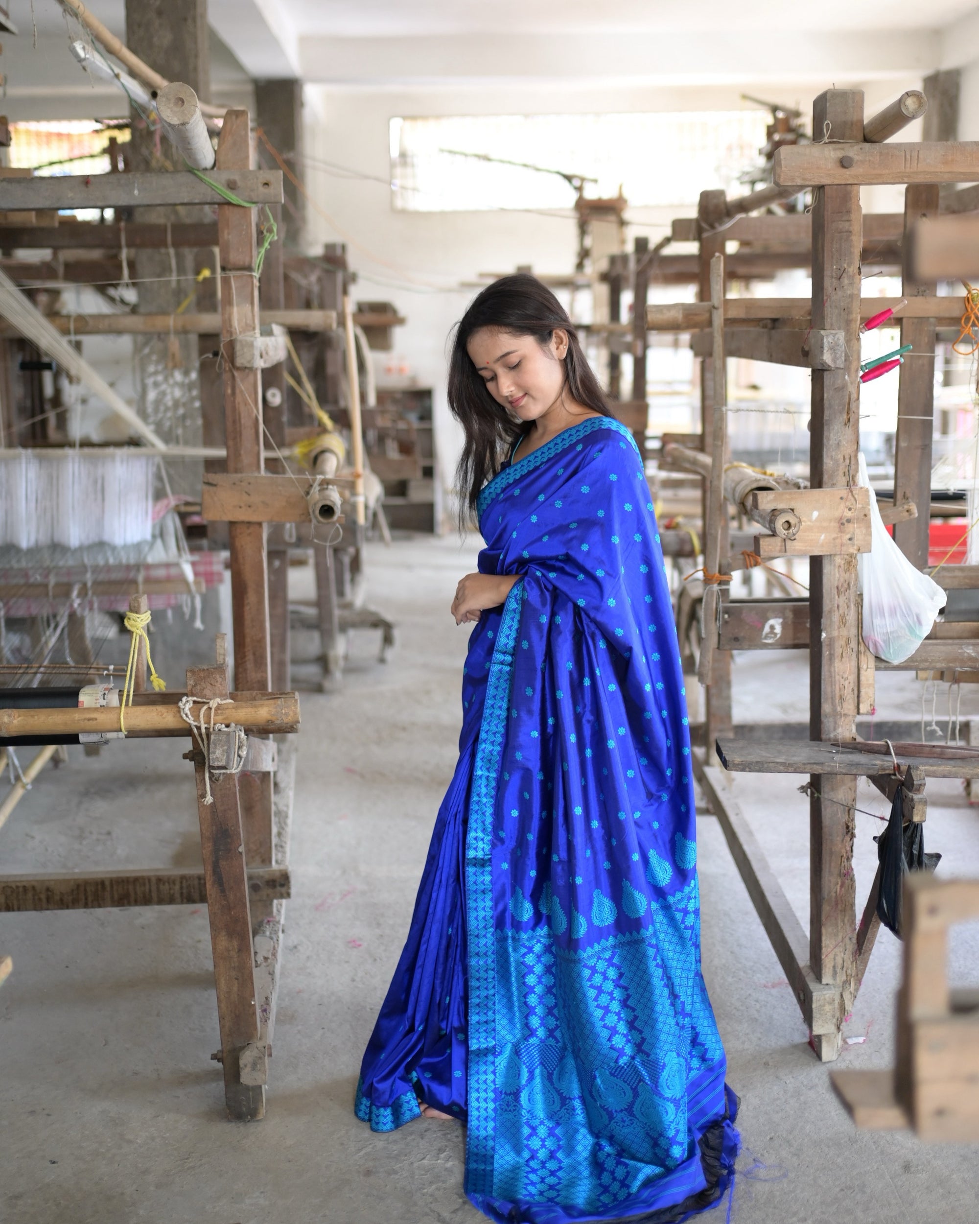 Full length in the aisle between handlooms, eyes lowered: the royal-blue drape scattered with turquoise flowers, the pleats and the turquoise border falling to the floor.