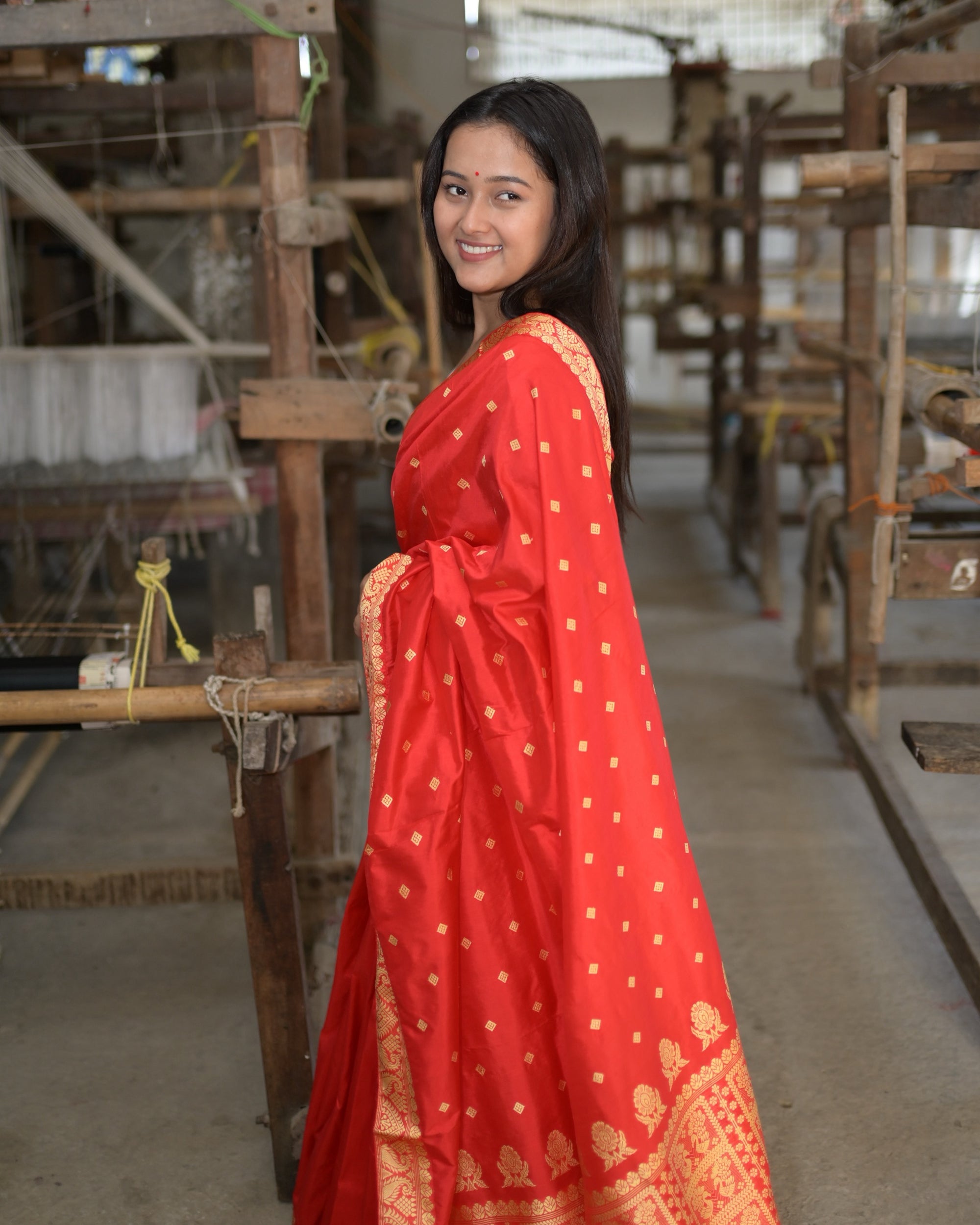 Smiling back over the shoulder, the pallu falling down the front: golden squares on red and, at the hem, the golden figures of the pallu.