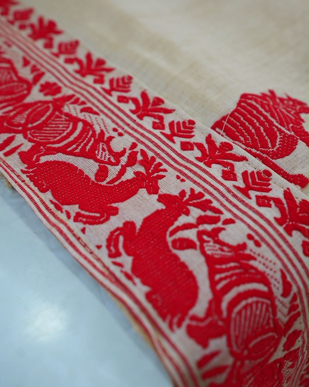 The border close, running across a fold: red rhinoceros and deer between slim stripes and a line of leaf sprigs, with a body rhinoceros on the cream beyond.
