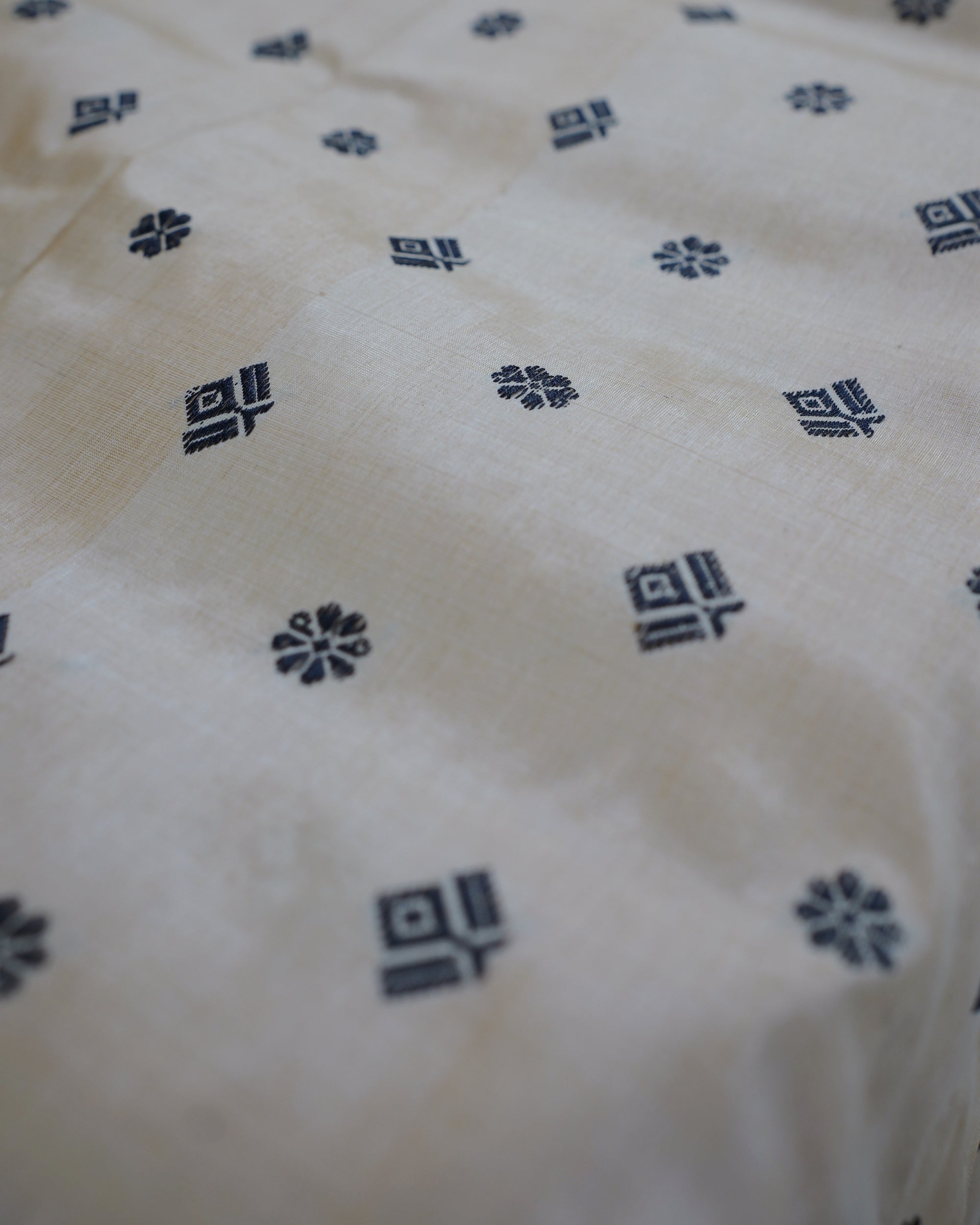 The body close, the cloth softly creased: small black stepped diamonds and eight-petal flowers on cream, sharp across the middle of the frame and soft towards the edges.