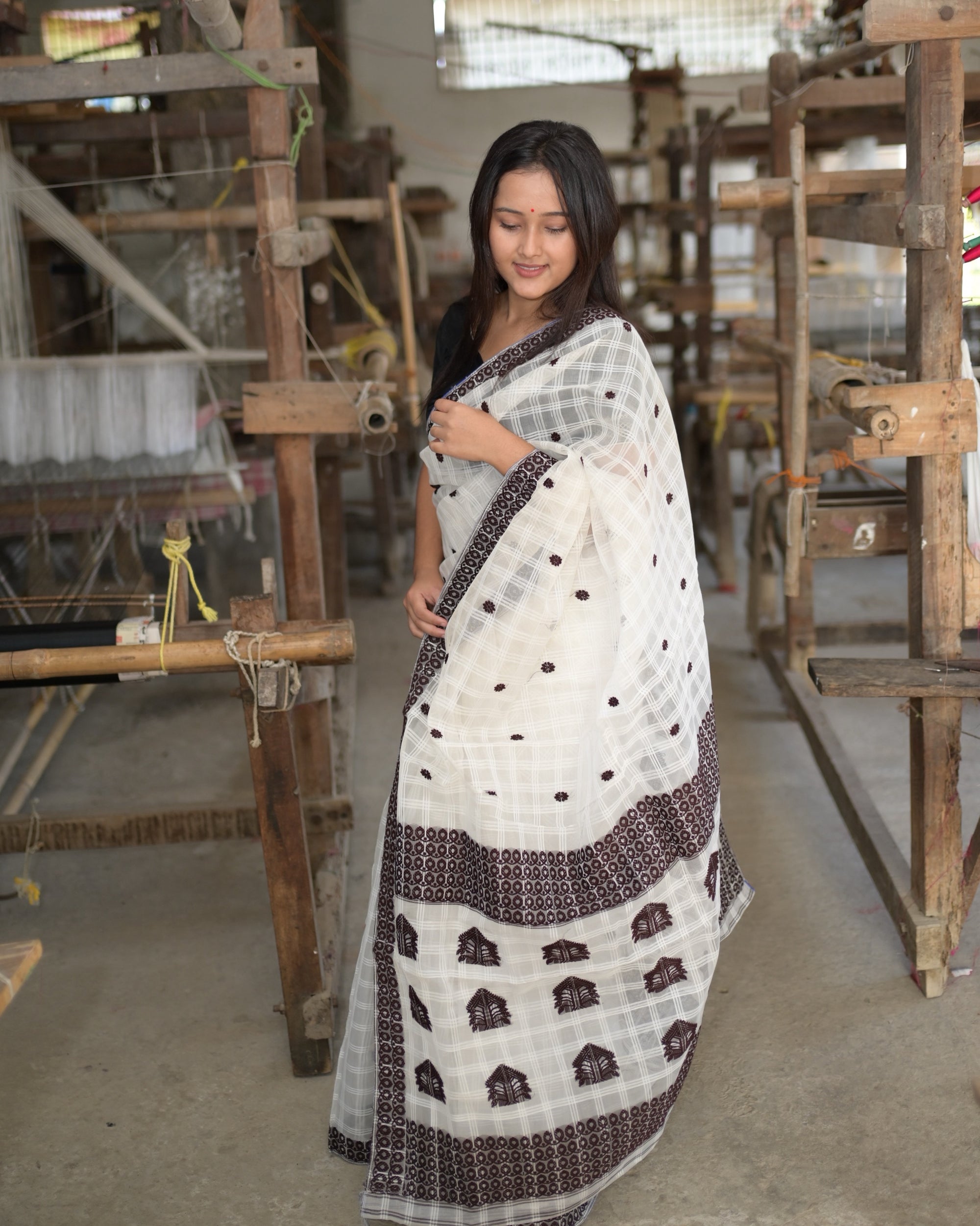 Looking down, one hand at the shoulder, the pallu spread in front: rows of large peaked motifs on the white check between two wide maroon bands of interlocking teardrops.