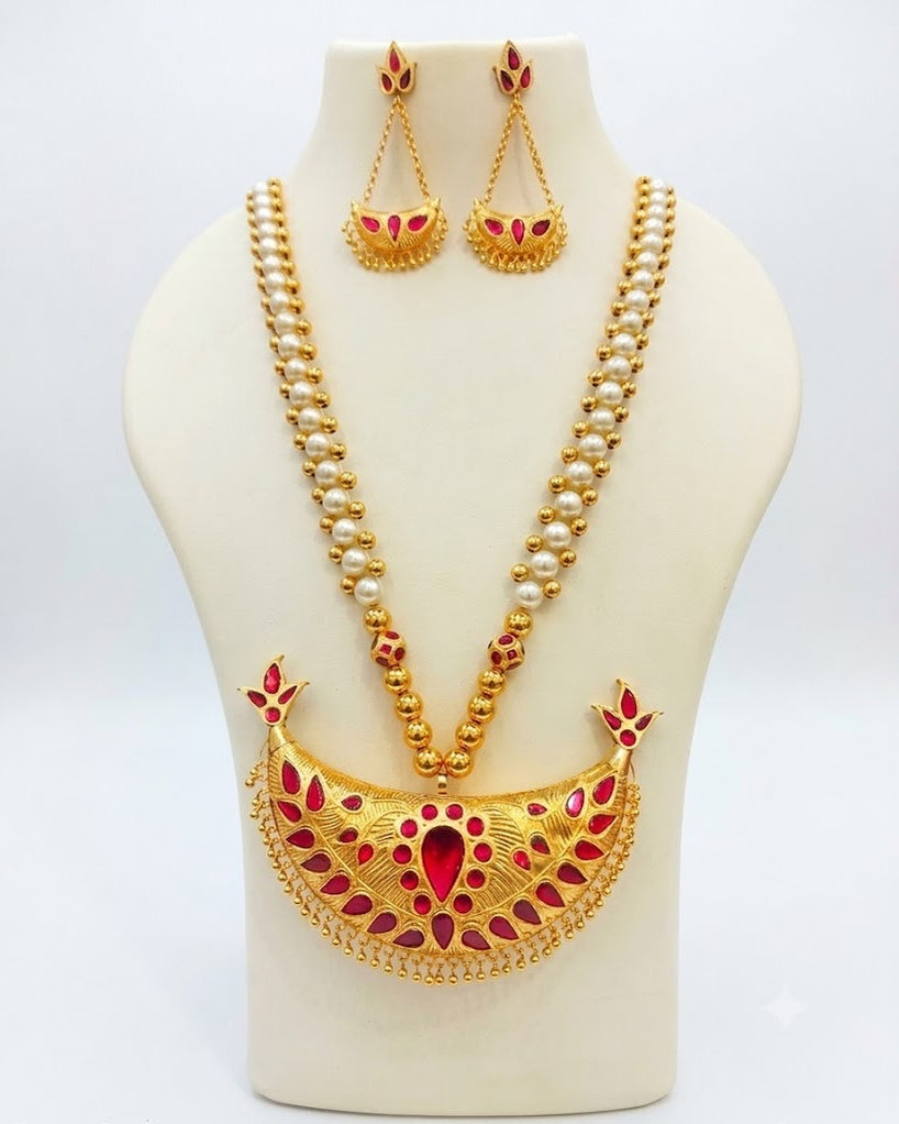 On a cream display bust against a pale grey ground: a wide engraved gold crescent set with red petal stones around a large red teardrop, fringed with small gold beads, on a chain of pearl-white beads between lines of gold beads. The earrings repeat the crescent, hung from a three-stone bud on two fine chains.