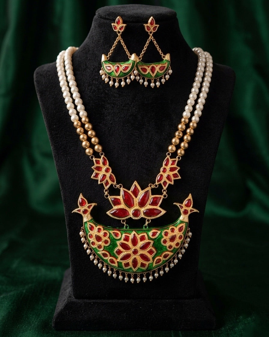 The necklace and earrings on a black velvet bust against a dark green velvet drape. Two strands of white pearl-like beads turn to gold beads and red lotus links, and a larger red lotus hangs a crescent with a bright green face, set with a six-petal red flower between two smaller rosettes and fringed with white drops. The earrings are small green crescents with three red stones and white drops.