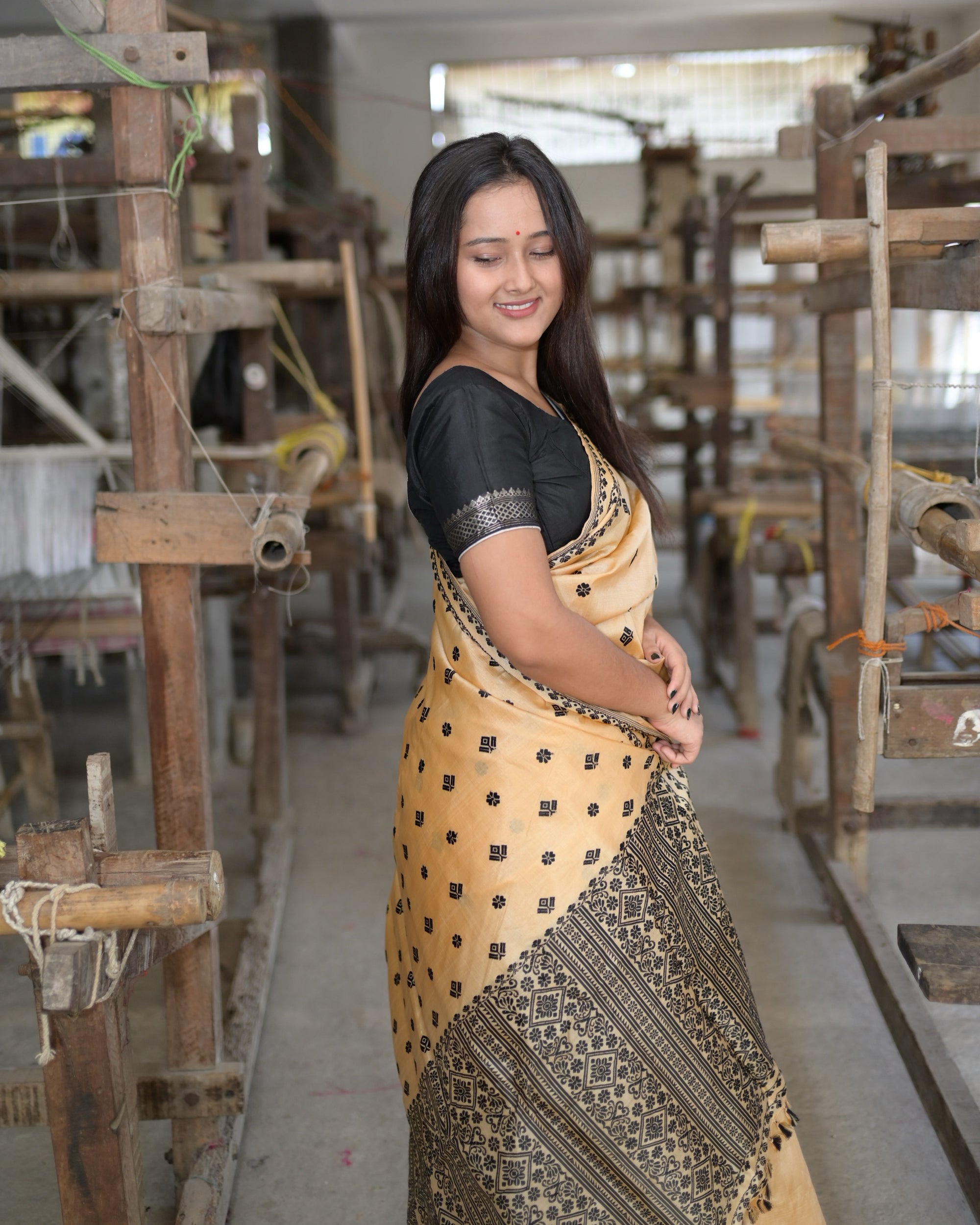 Knee up in profile, eyes closed and smiling, in a black blouse banded at the sleeve: black flowers and squares on golden beige over the black columns of rosettes and diamond medallions in the pallu.