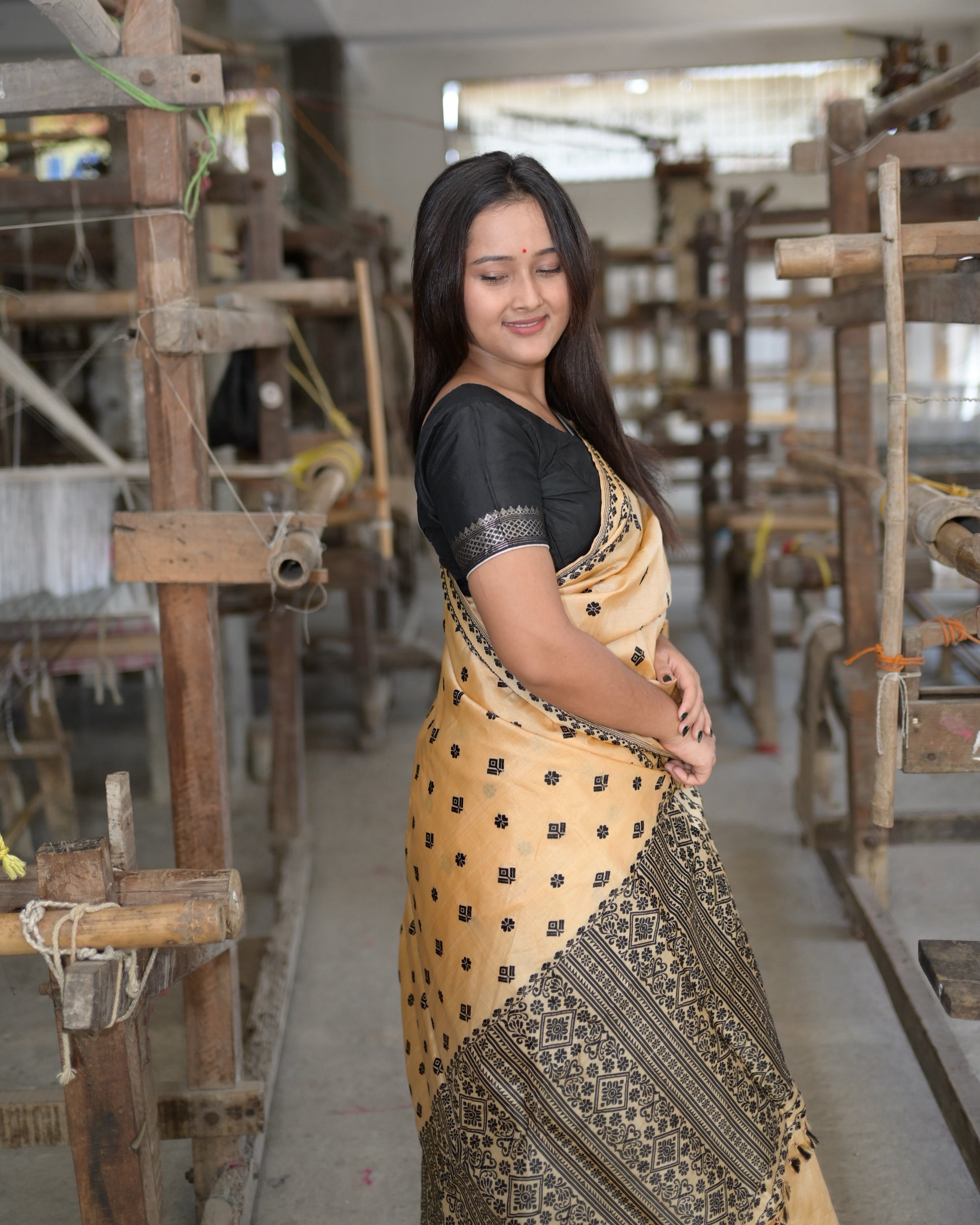 Turning away with a smile, hands together at the waist: the black panel of the pallu wrapped across the lower body.