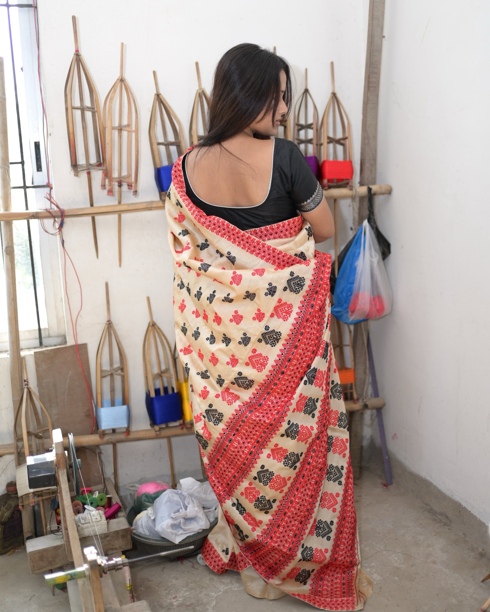 From behind, in a black blouse: the pallu over one shoulder and down the back, red and black buti on cream, the red scroll border along its edge and rows of medallions at its foot.