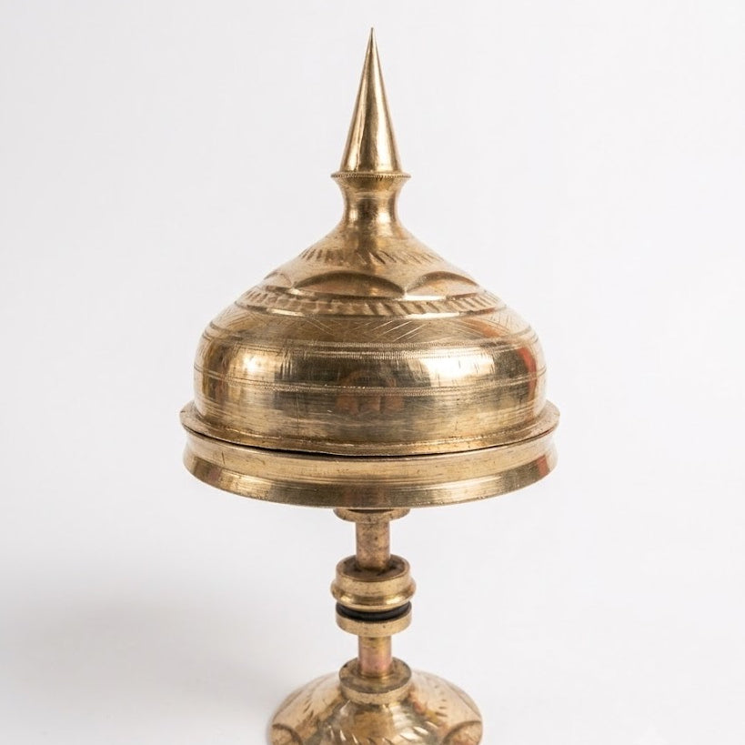 The xorai with its lid on, against white: a spired lid on a domed cover over the tray, a turned stem with collars and a flared foot, all in burnished brass.