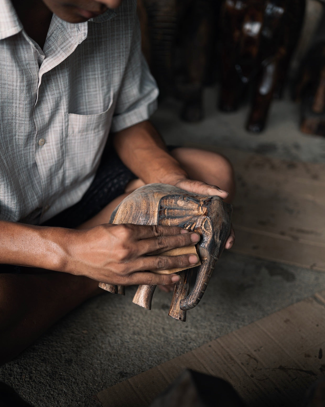 Two hands rubbing a small carved elephant smooth on the workshop floor.