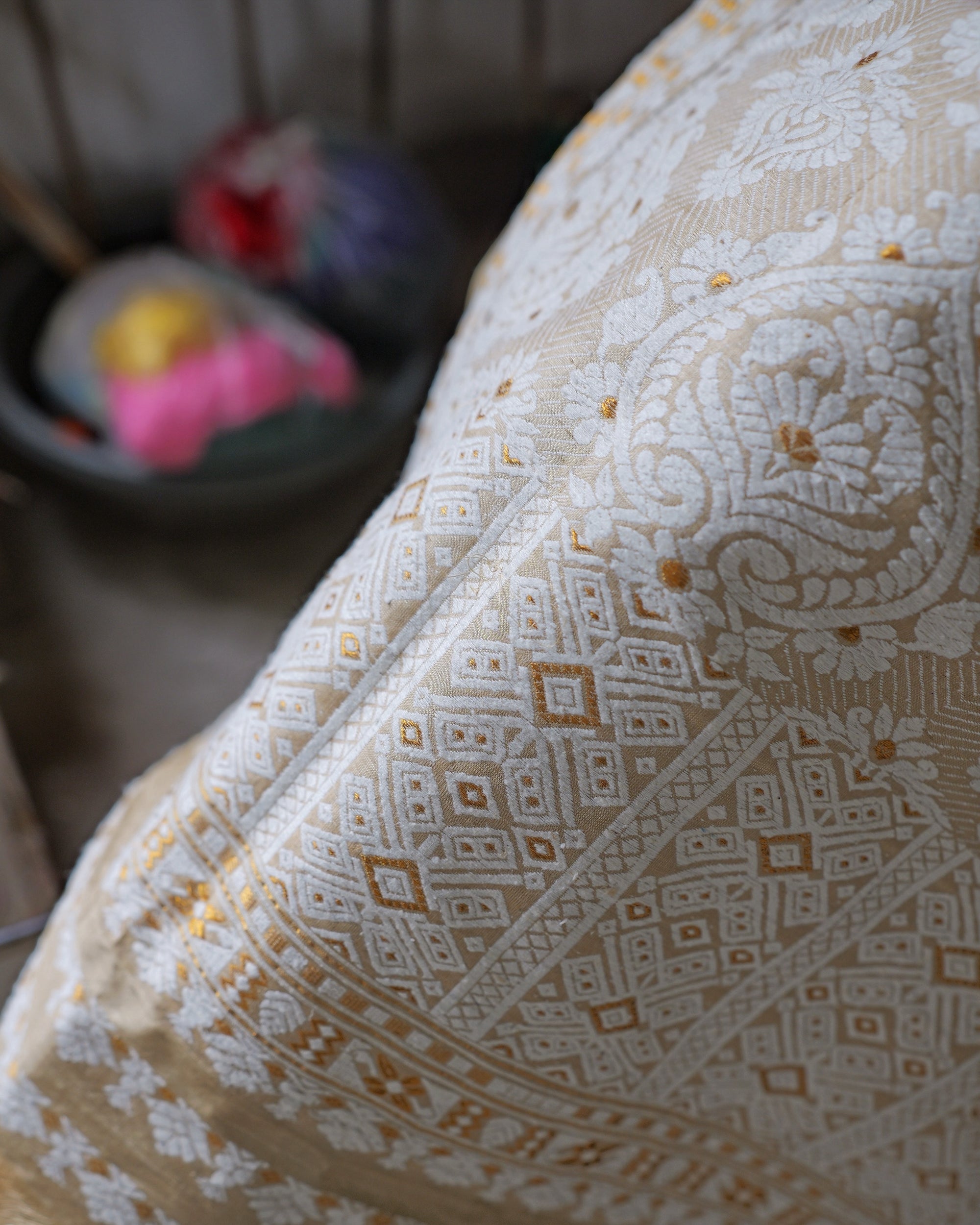 The pallu close, folded over the knee: ivory paisleys filled with flowers beside diagonal bands of diamond lattice, dotted with golden-orange.