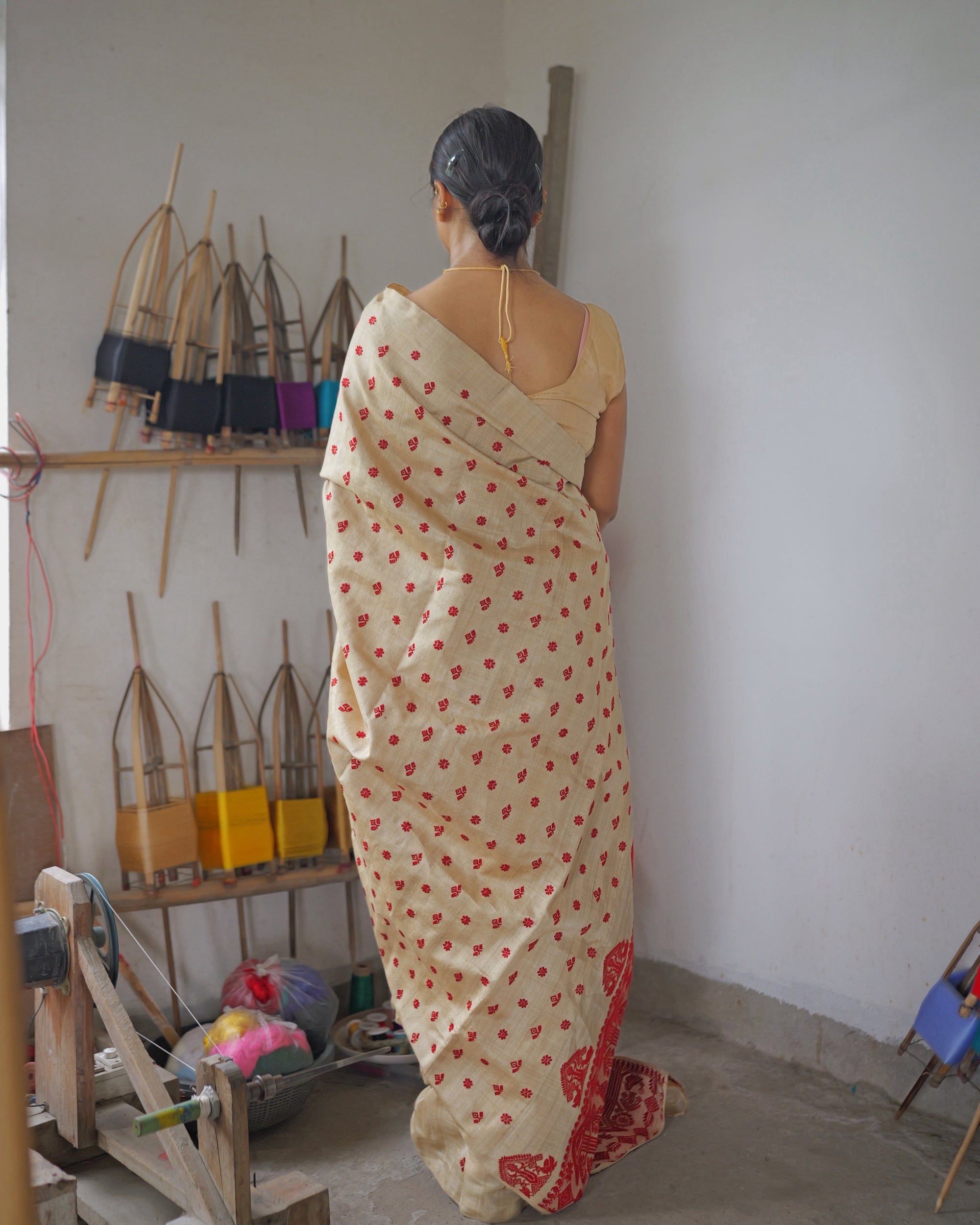 Seen from behind, standing by the wall of bamboo reels, the saree falling full length down the back to the red pallu at the floor.