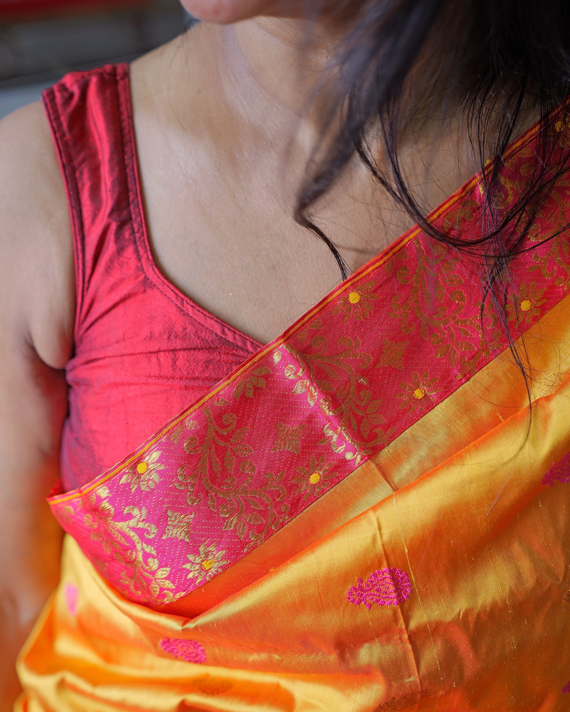 The pink border crossing the chest from the shoulder, gold creeper and yellow-centred flowers on it, over a red sleeveless blouse; a pink kalka on the marigold body below.