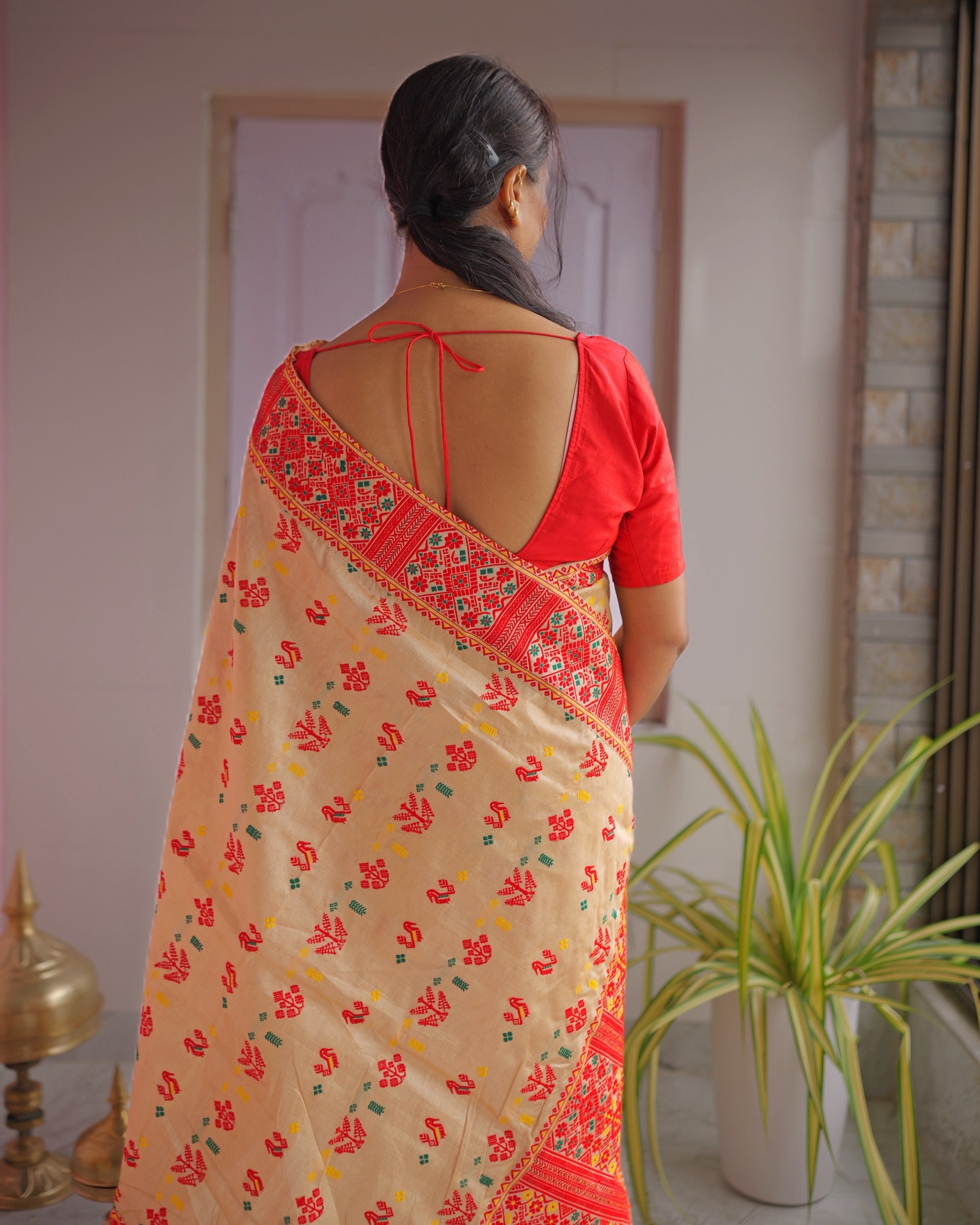 Seen from behind in a red blouse tied at the back, the drape falling down the back. Red birds and trees across the beige ground, with the red lattice border over the shoulder.