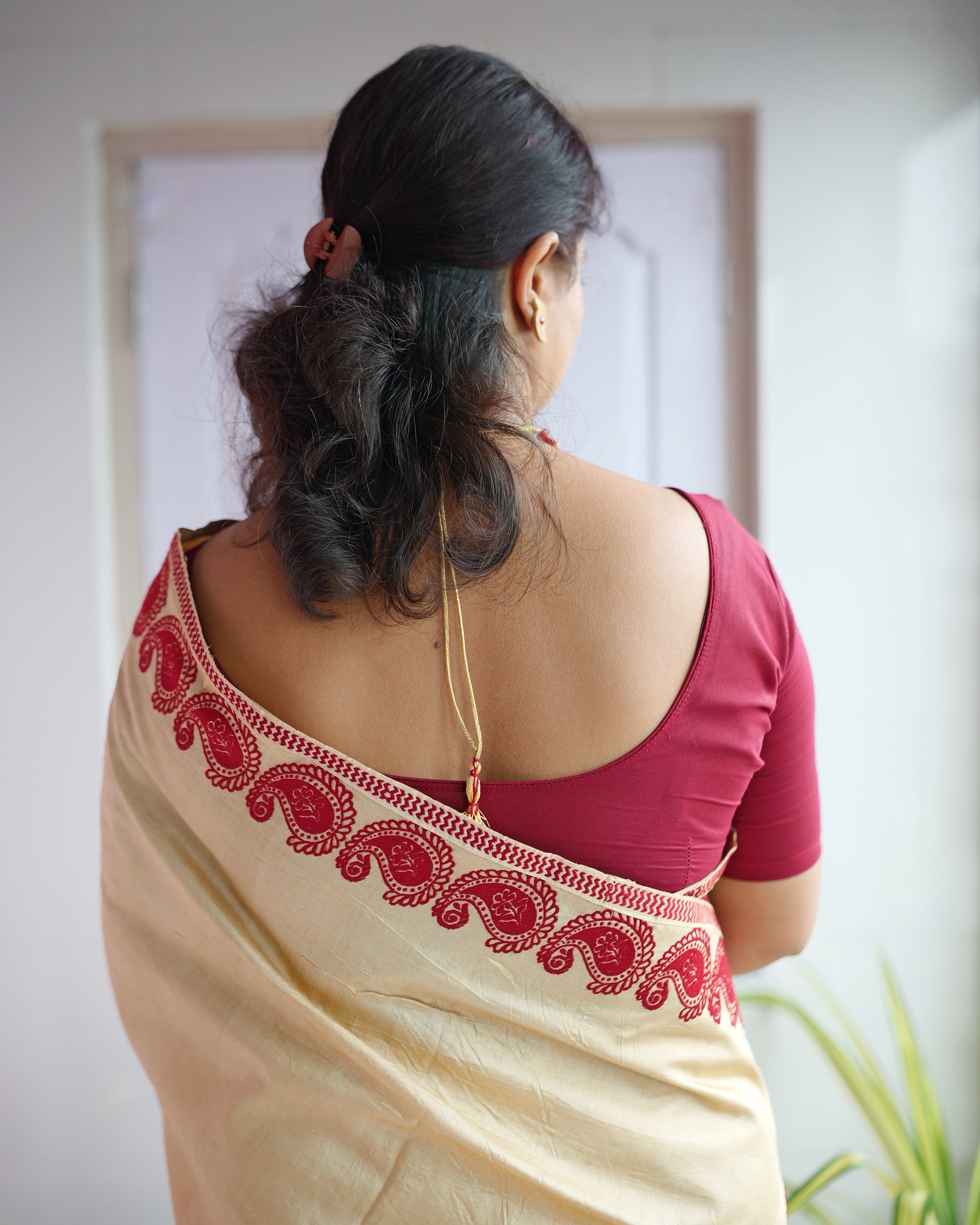 Seen from behind, the border running over the shoulder. Red paisleys and a fine dotted band against the cream ground, over a maroon blouse.