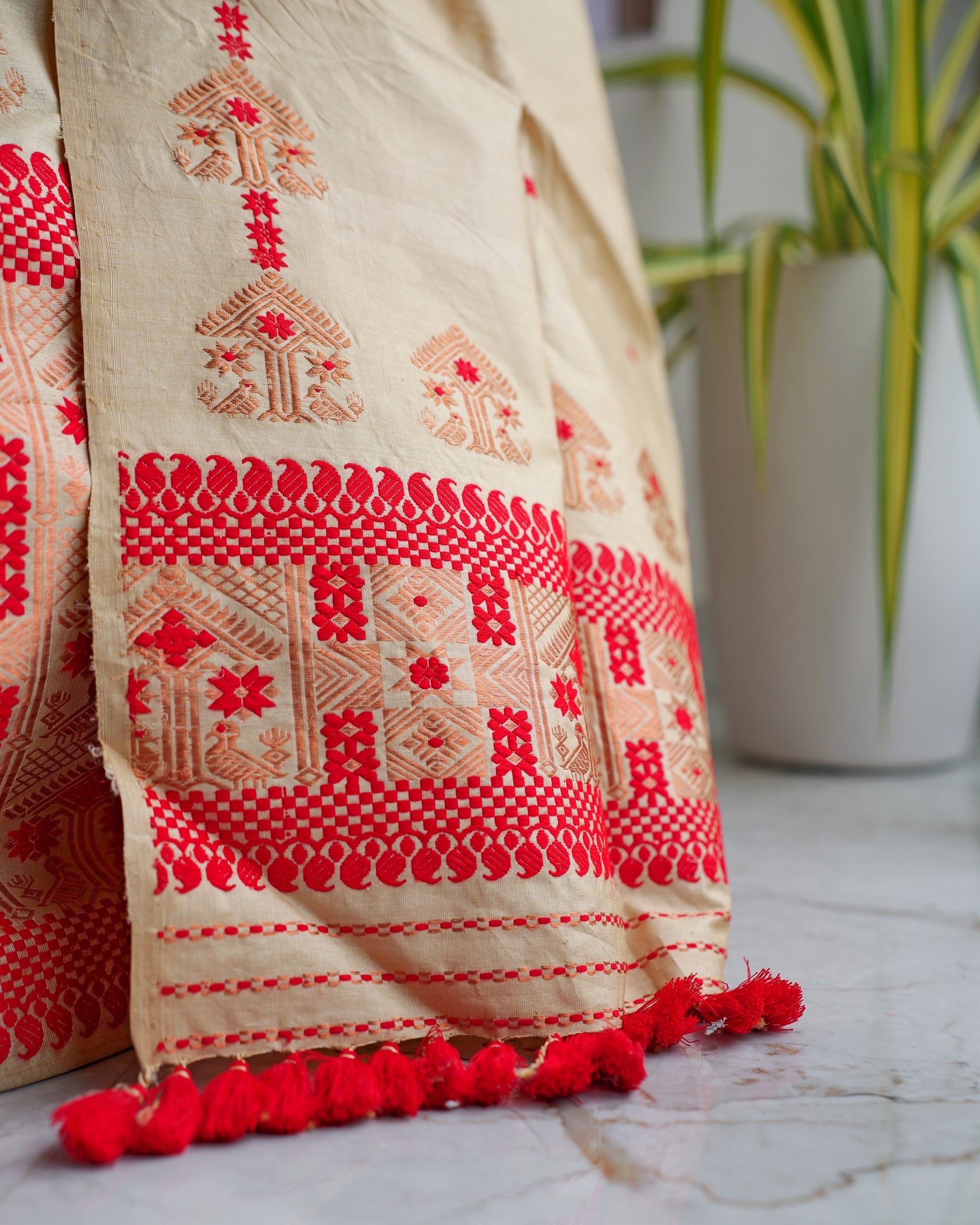 The sador end close up. Roof-shaped motifs above a red scallop band, a panel of geometric blocks and stars, fine red stripes and plump red pom-pom tassels resting on a marble floor.