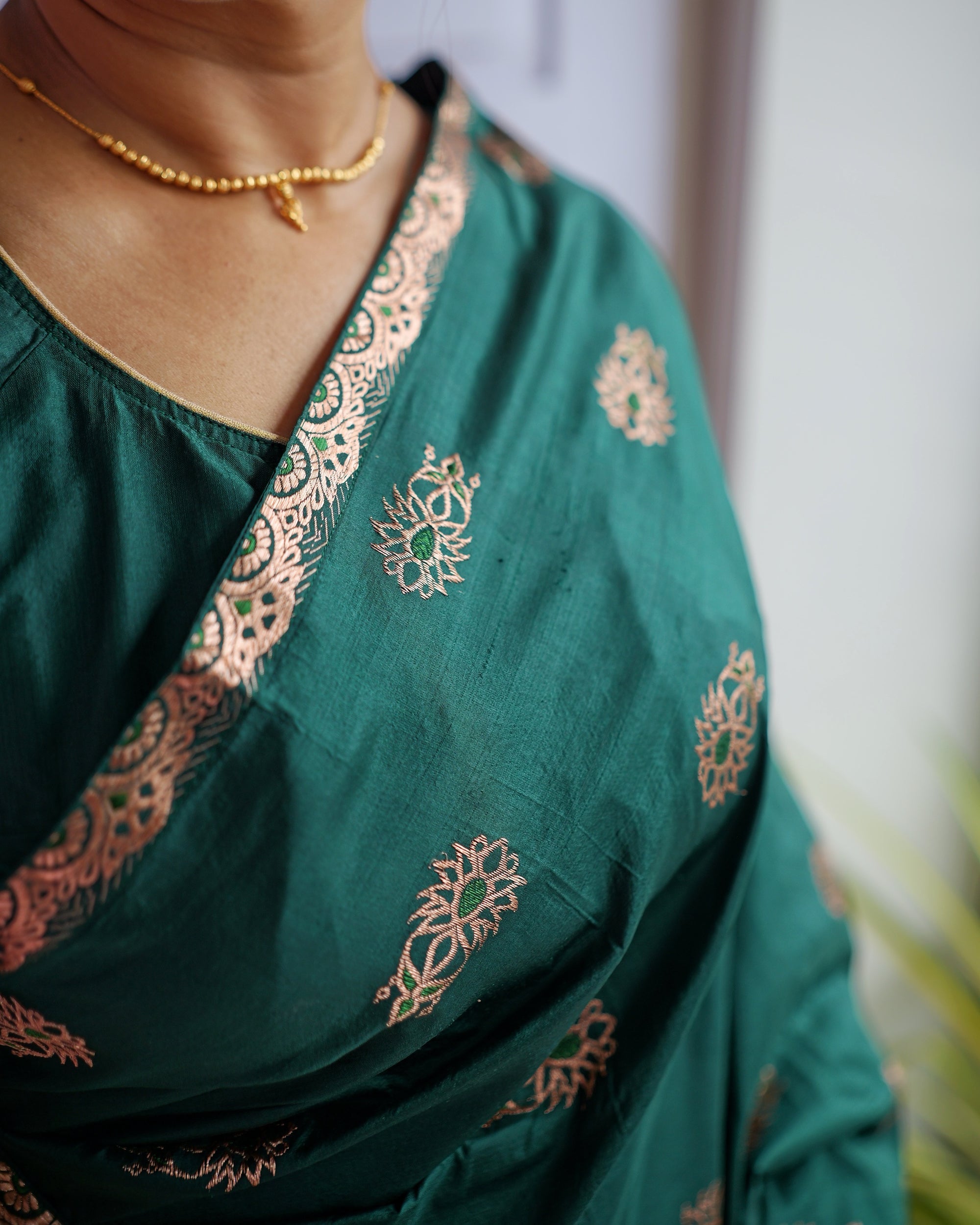 The border across the collarbone, worn with a thin gold necklace. Rose-gold floral buti on emerald, edged with a scalloped zari band.