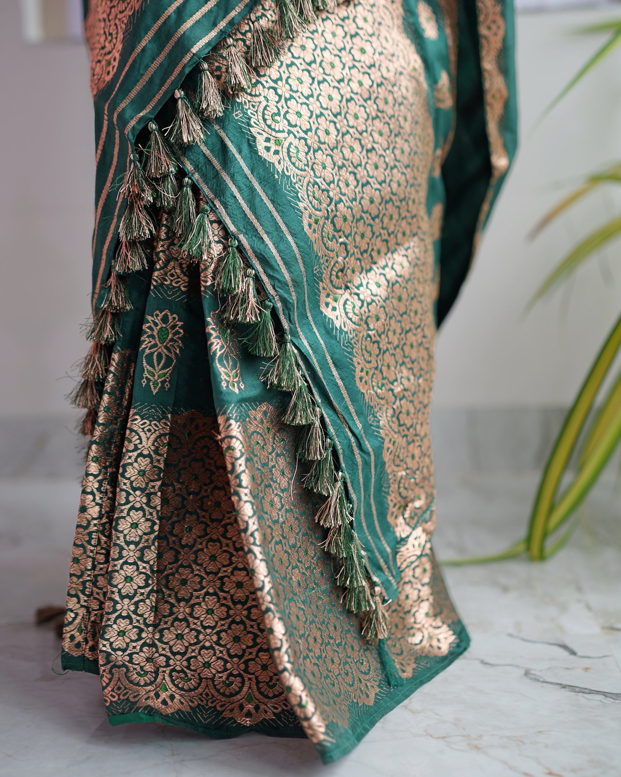The striped sador end hanging over the mekhela hem, a line of green and gold tassels beside panels of rose-gold rosette lattice.