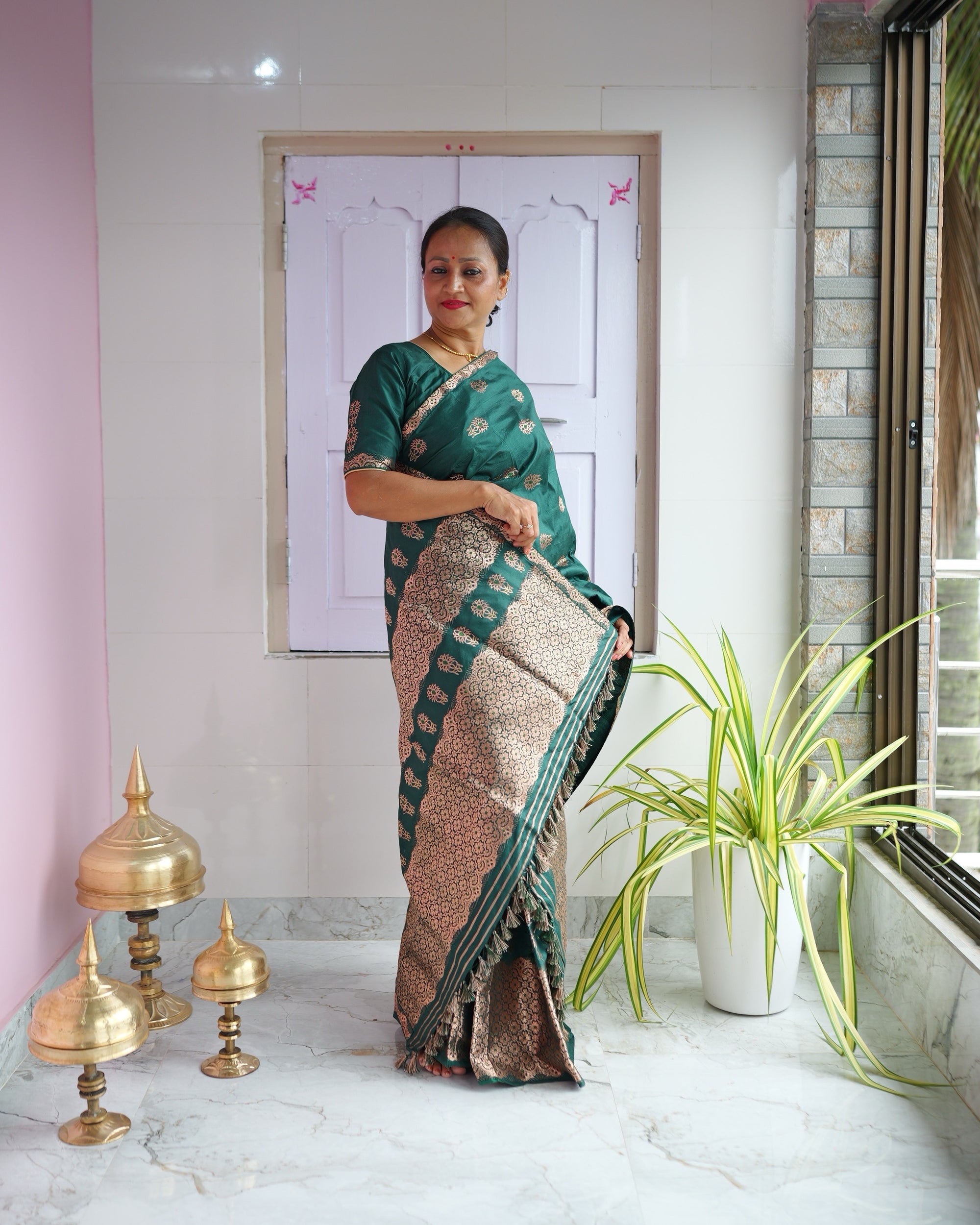 Standing on a verandah with a pink wall and brass xorai on the floor, the set seen full length.