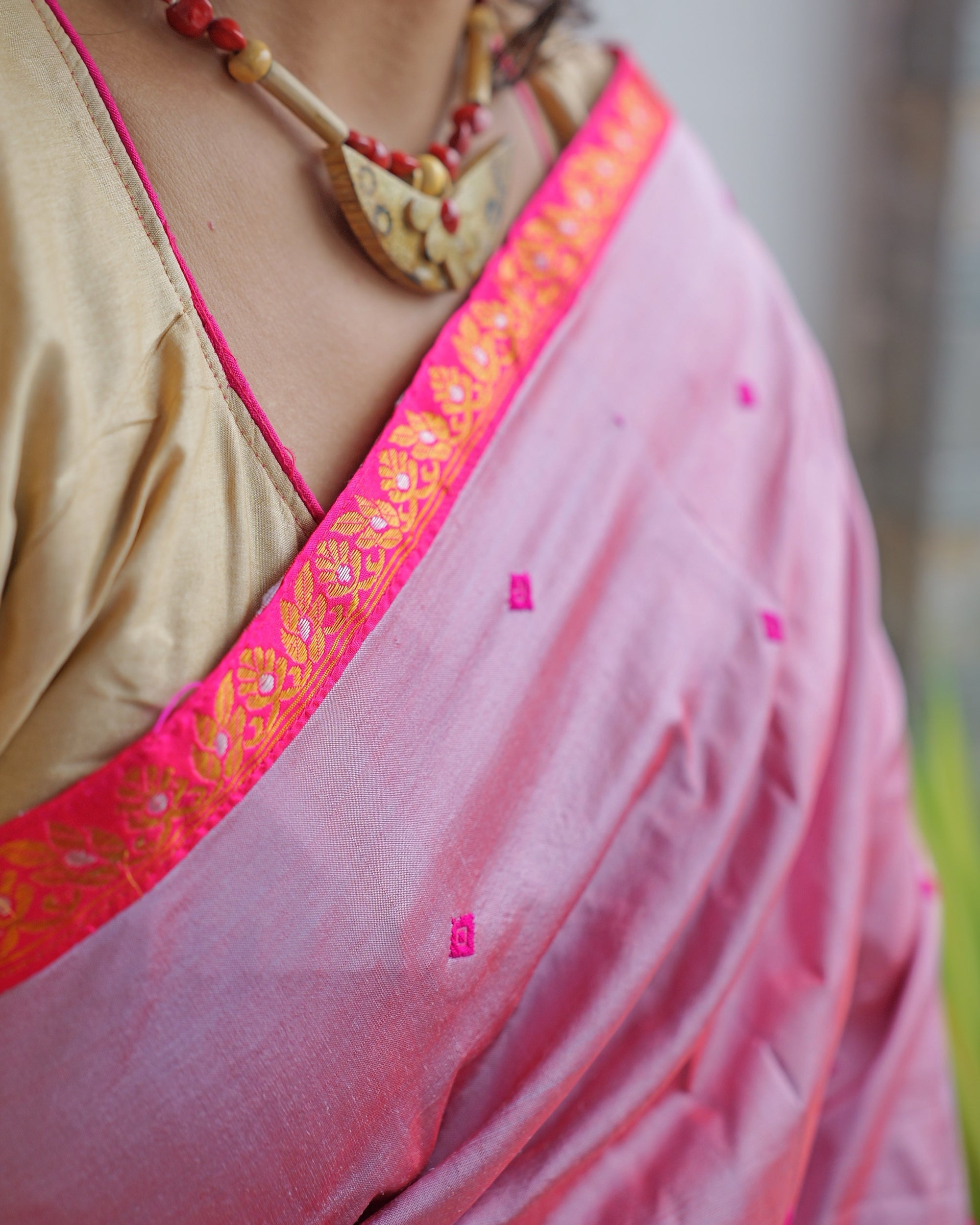 The border across the collarbone, worn with a cream and red bead necklace. A golden-orange zari band of small florets edging the rose-pink ground.