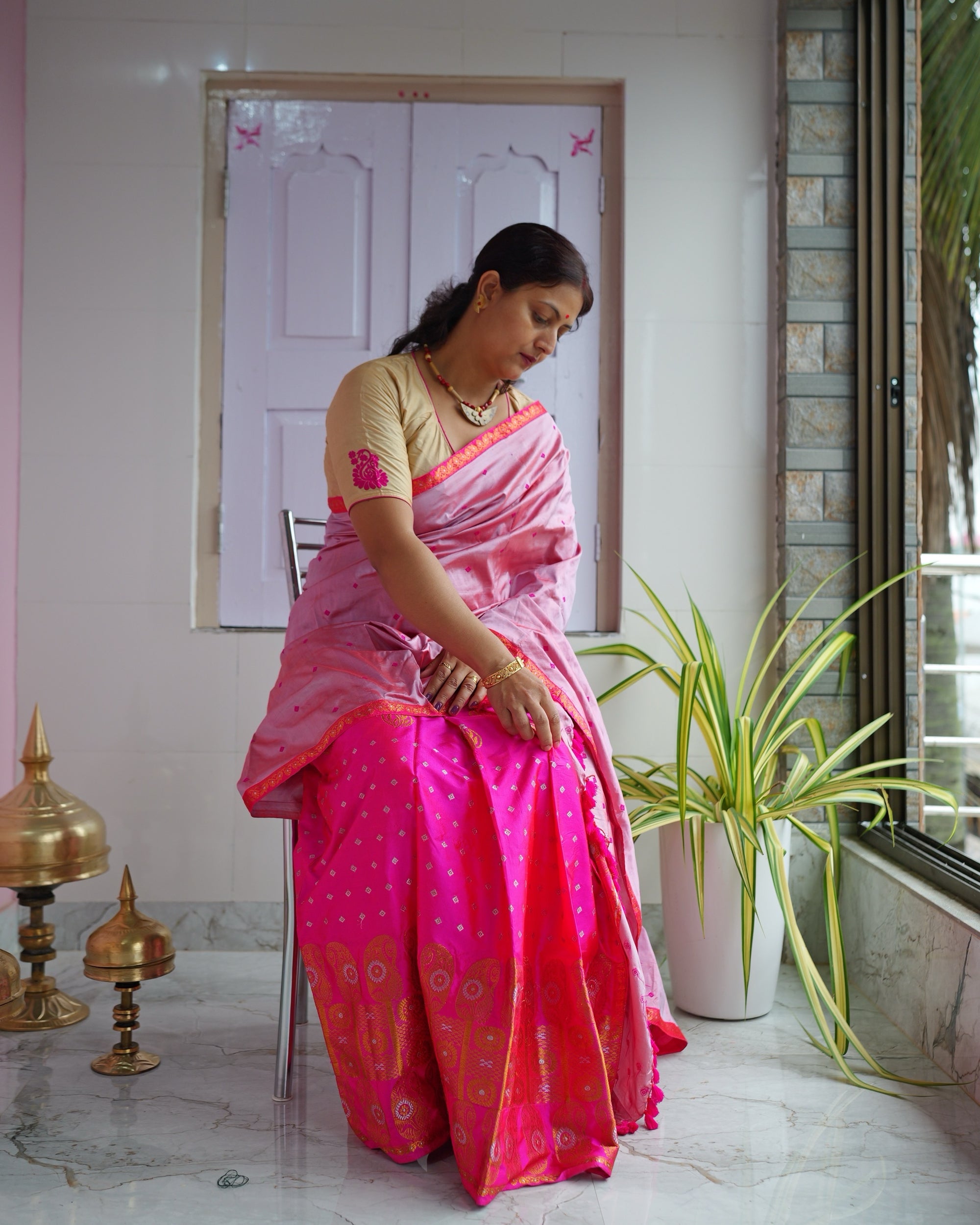 Seated on a verandah with a pink wall and brass xorai on the floor, the set seen full length.
