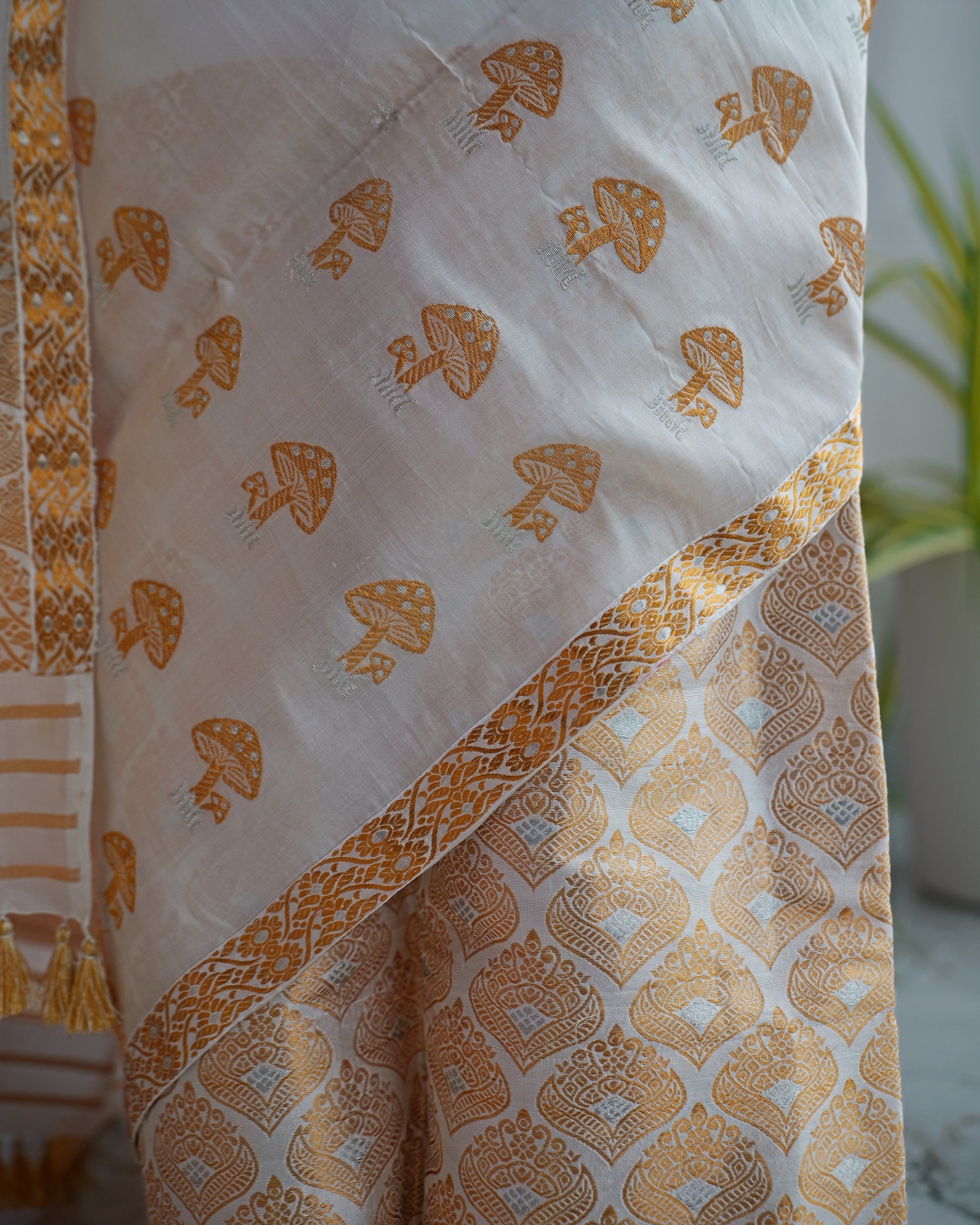 The mushroom motifs close up, each with a dotted cap and a slender stem, beside the gold-and-silver lattice of the hem.