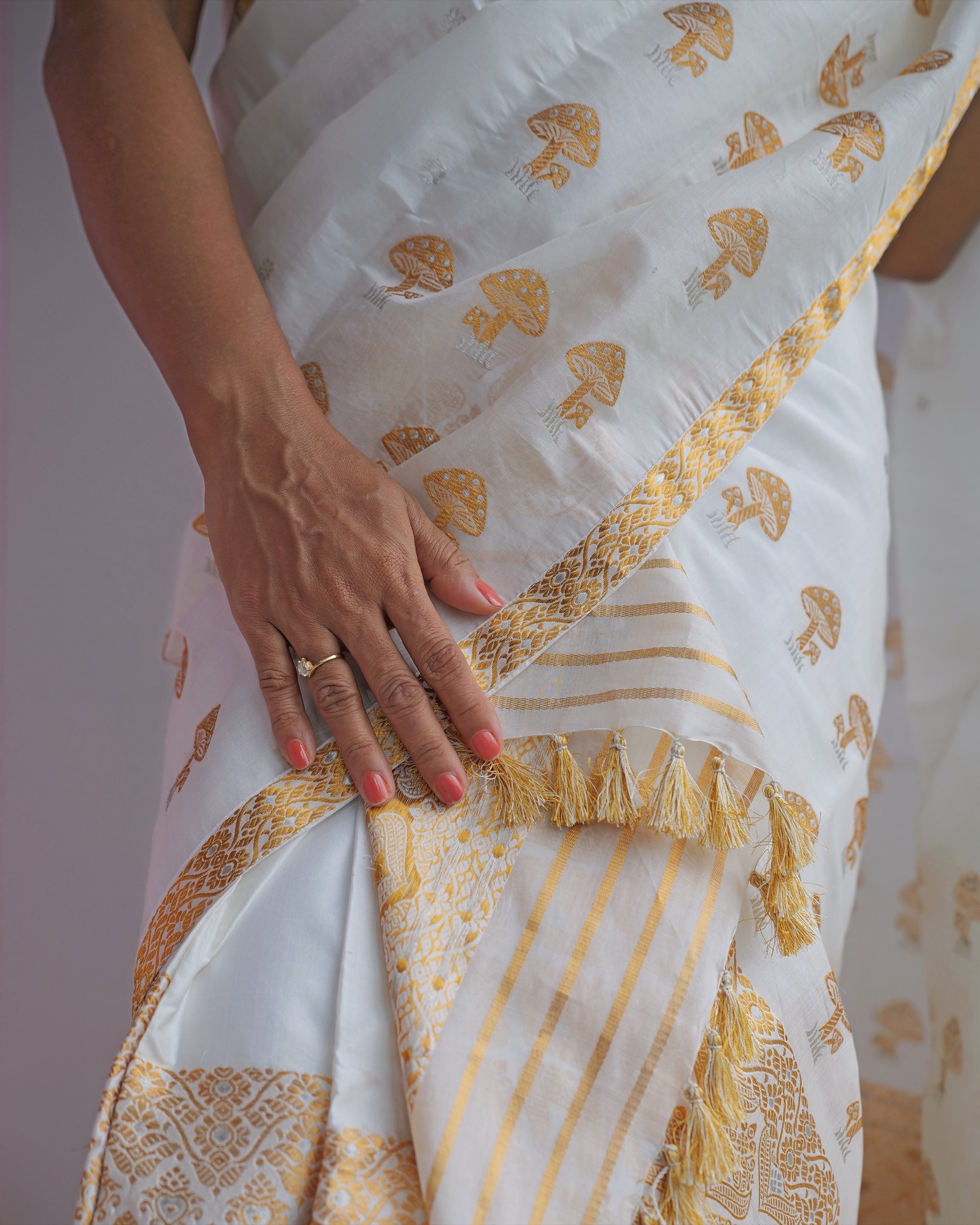 A hand resting on the drape where it crosses the mekhela, gold stripes and a row of gold tassels below.