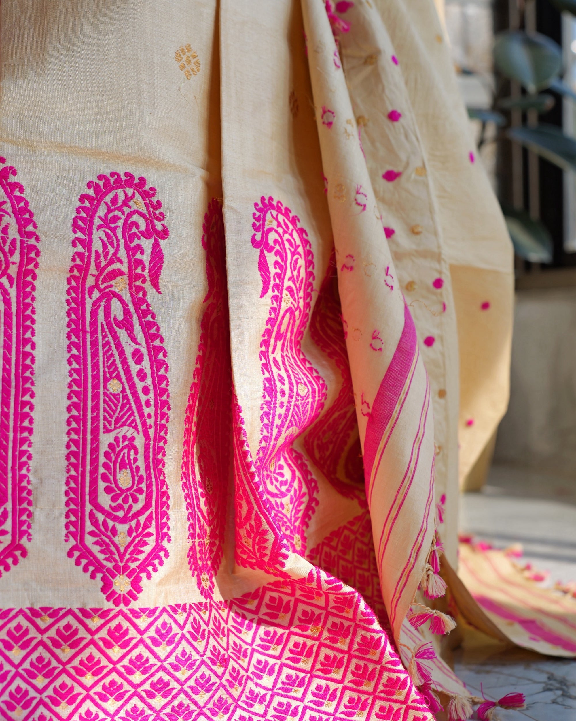 Two tall paisleys close up, filled with pink flowers and leaves and flecked with gold, above the border of diamonds; the sador hangs beside them, dotted in pink and gold, its striped end and tassels at the bottom right.