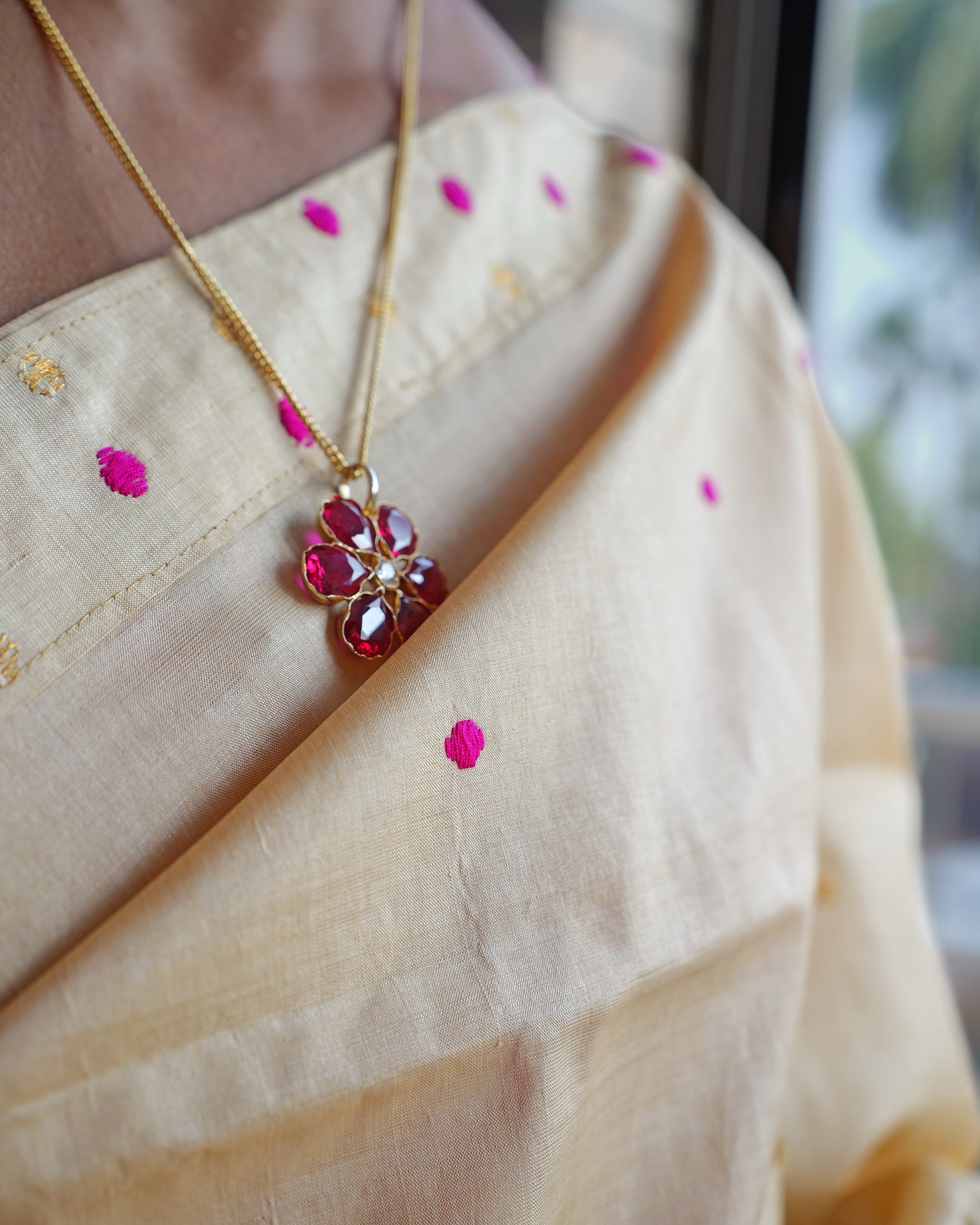 The drape across the collarbone, worn with a fine gold chain and a red-stone flower pendant. Pink dots and small gold motifs on the cream ground.