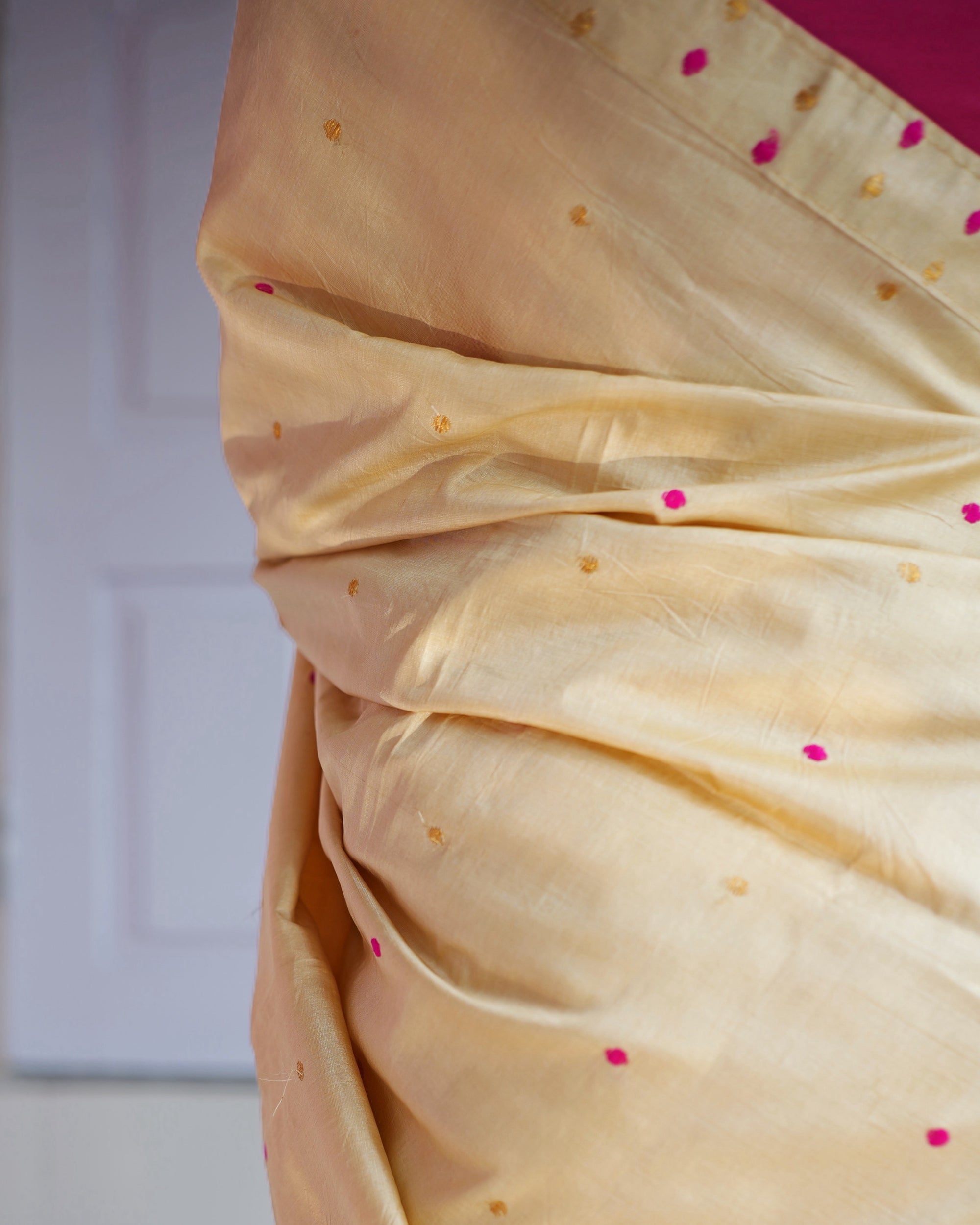 The drape in soft folds, pink dots and small gold motifs scattered across the plain cream silk.