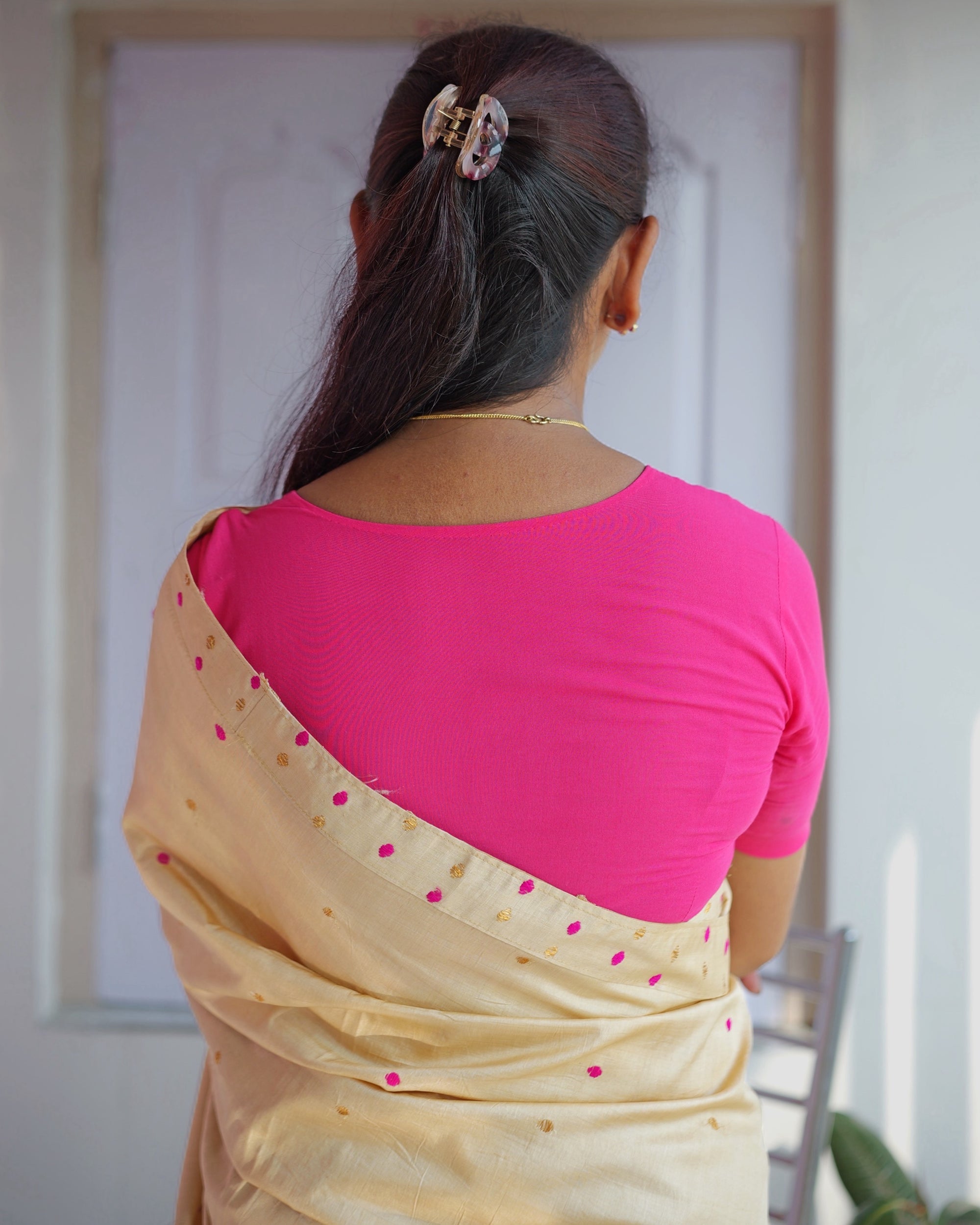 Seen from behind, a rani pink blouse with the sador laid over the shoulder, its edge lined with pink dots and small gold motifs.