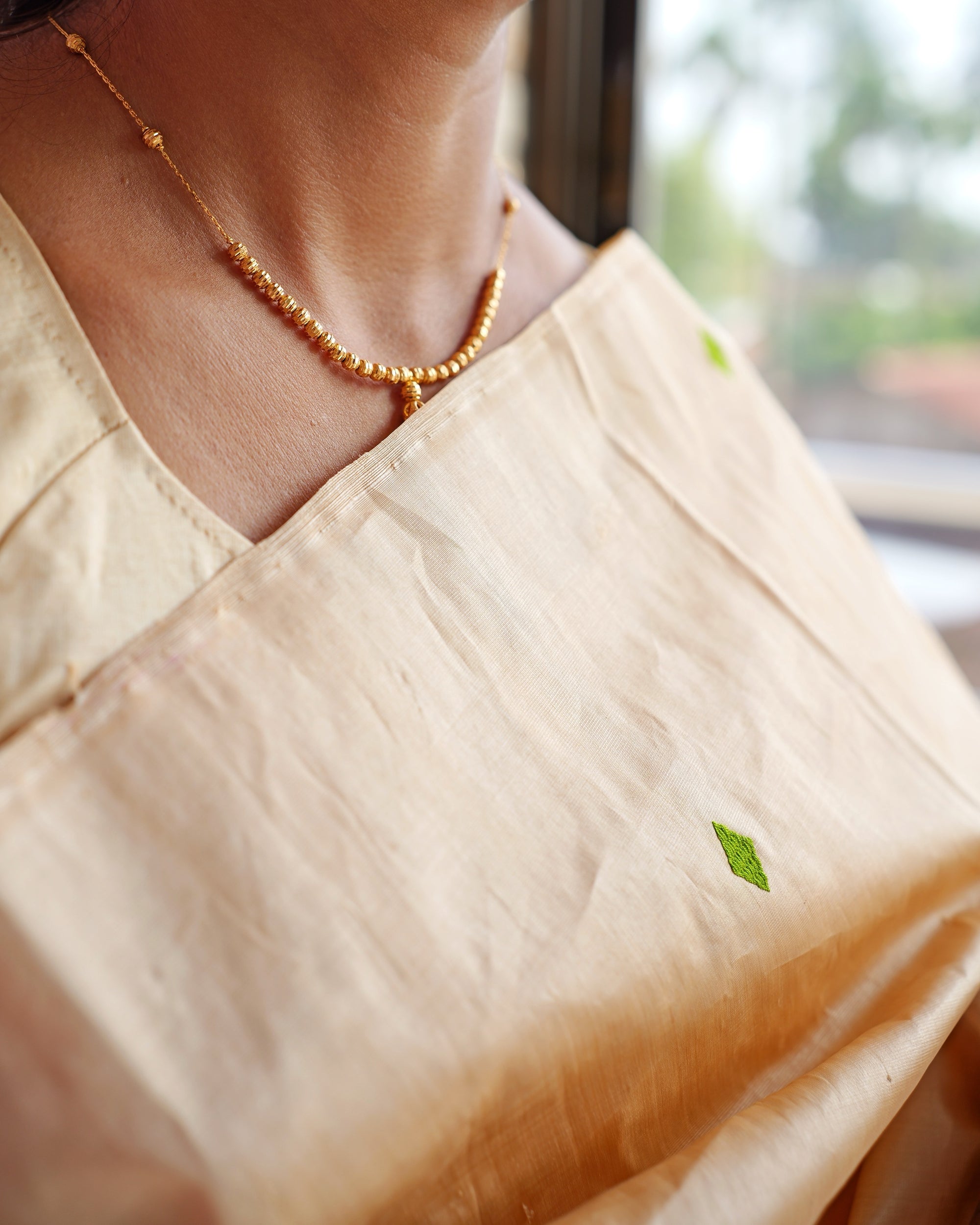 The drape across the collarbone with a fine gold bead necklace. A small green diamond on the golden-beige silk, slubs running through the weave.