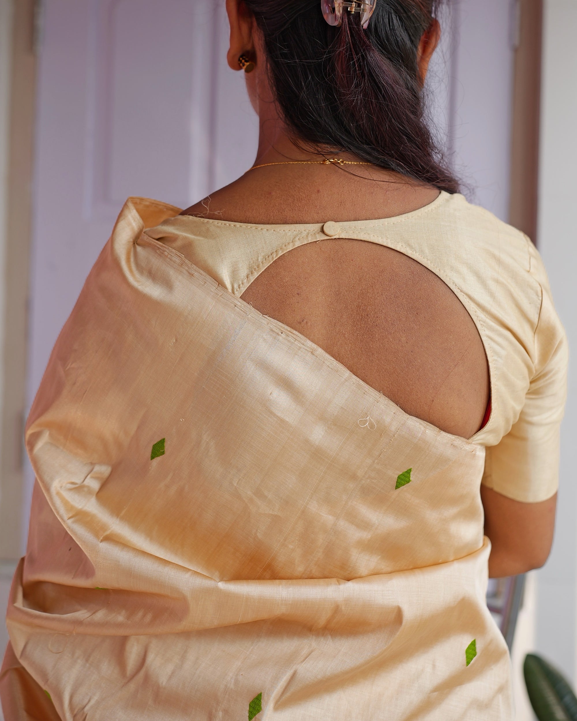 Seen from behind, a golden-beige blouse with a round open back, and the sador over the shoulder scattered with small green diamonds.