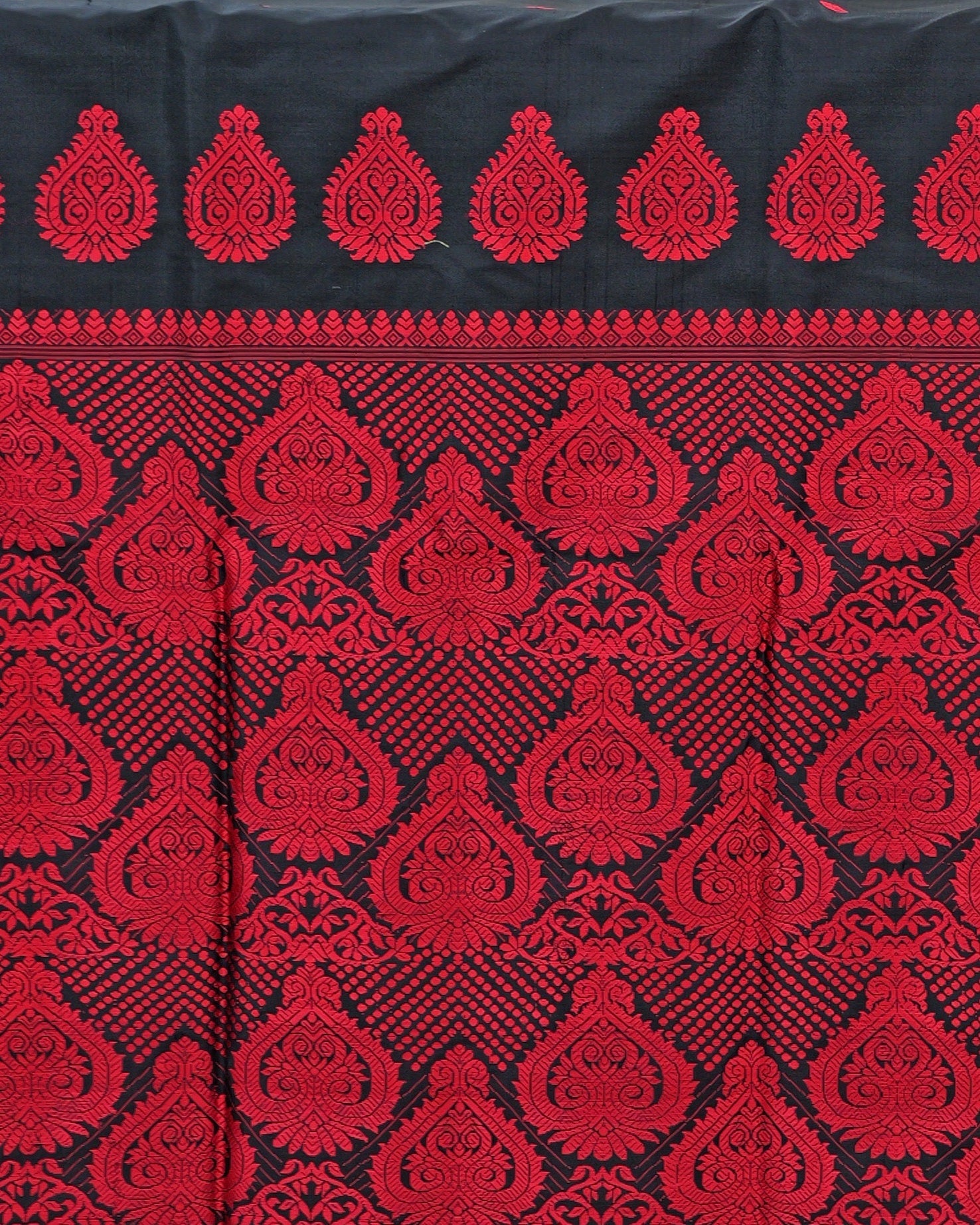 The pallu laid flat and photographed straight on: red teardrop medallions in a row across the black at the top, then staggered rows of larger scrollwork medallions with chevrons of red dots and small vines between them.