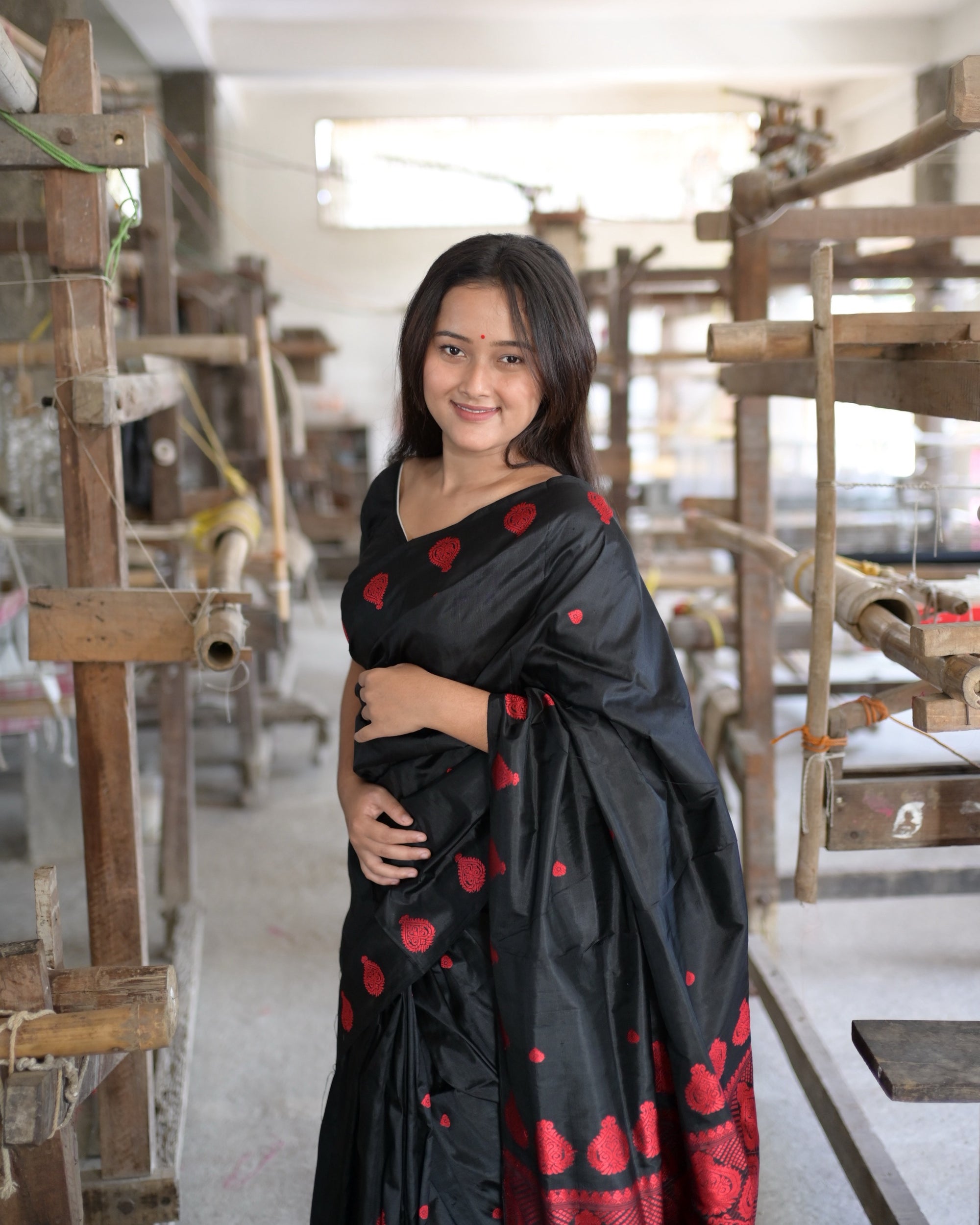 Waist up, smiling, a hand at the waist: red teardrop motifs on the black drape and the red pallu over the shoulder.