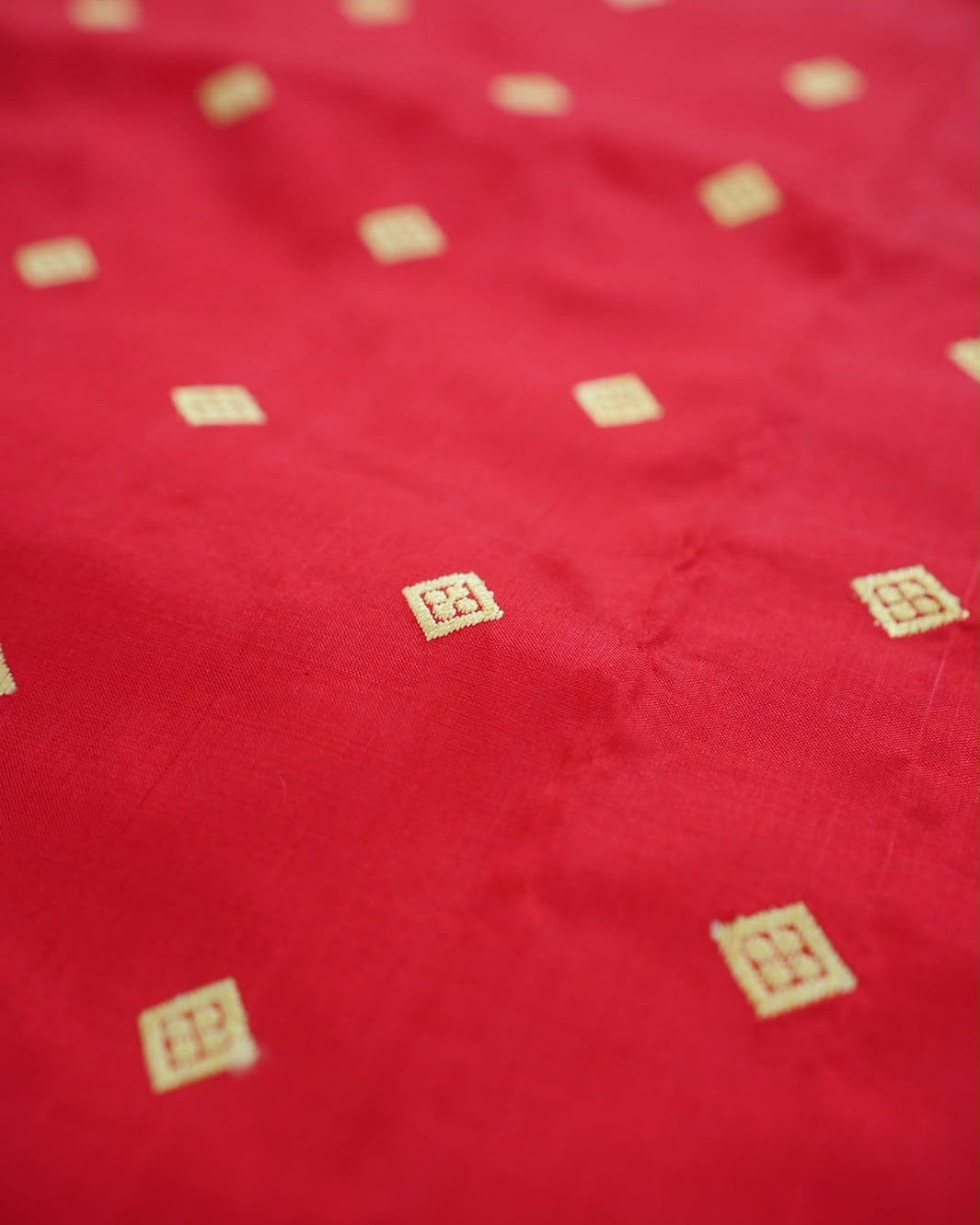 The red body close up and in shallow focus: small golden squares, each like a window with four dots inside, spaced across the silk.