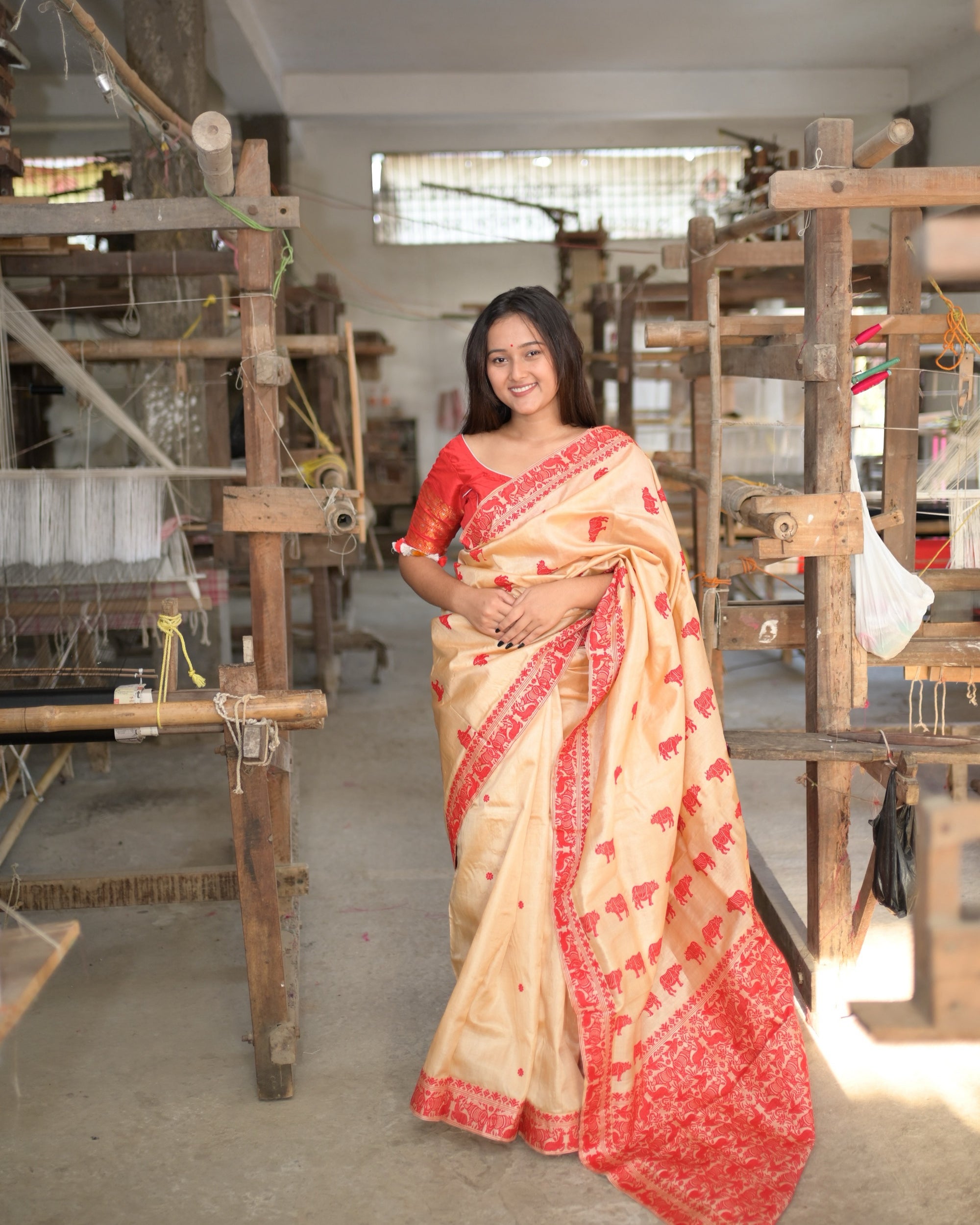 The whole saree from a few steps back, between two rows of handlooms: the red border, the rhinoceros buti and the red pallu edge on cream, worn with a red blouse.