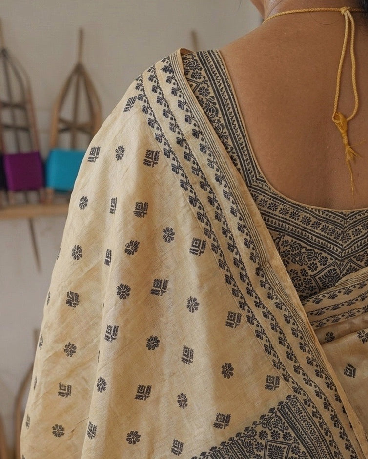 From behind, over one shoulder: rows of small black diamonds and flowers on the cream drape, a black border along its edge, and a blouse patterned in black at the back.