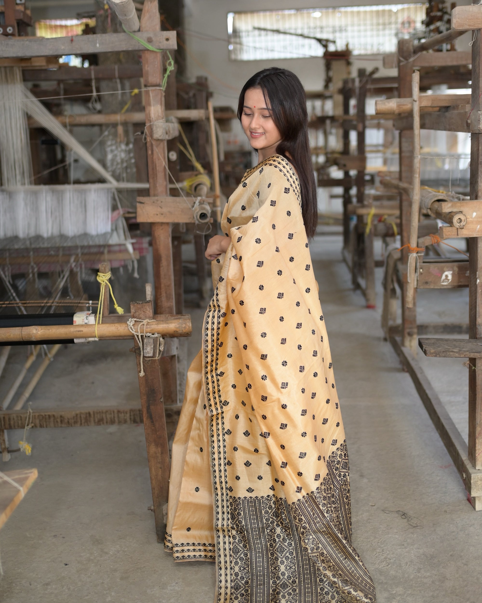 Turned to one side and looking down: the golden drape full length and the black panel of the pallu along the hem.