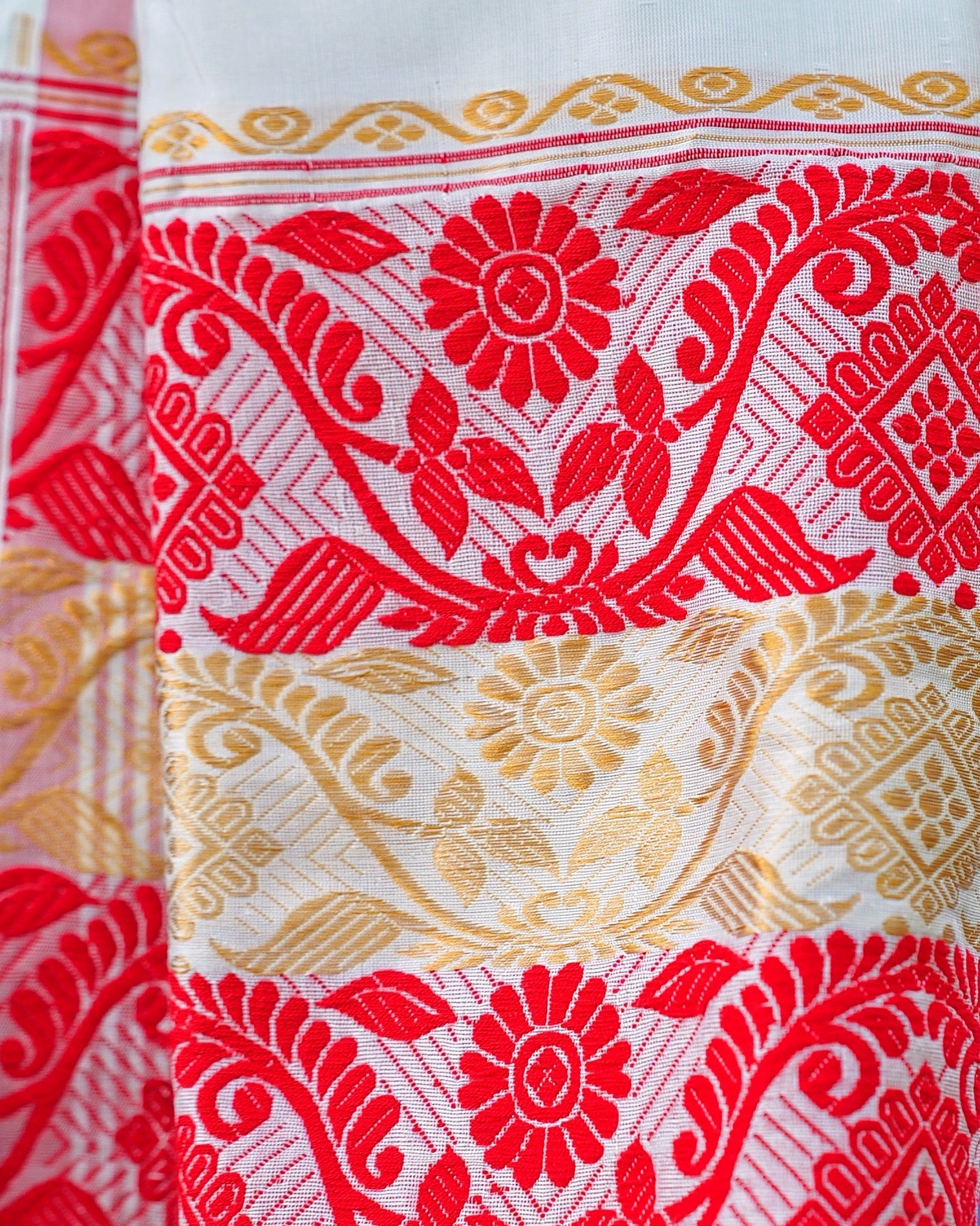 A woven end panel close up: red and gold-coloured creeper bands with flowers and leaves, the motif yarn lying in raised floats over a plain ivory ground.