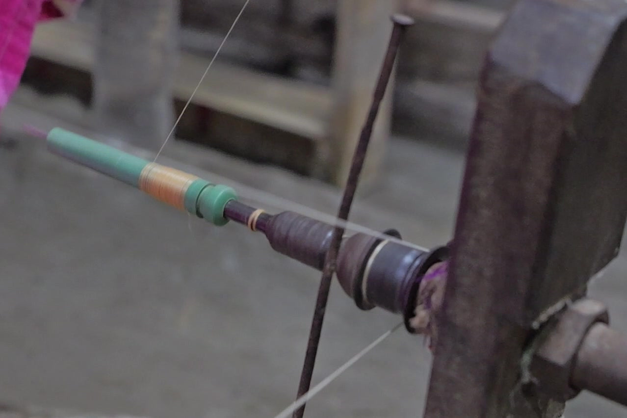 A green plastic pirn on a spindle filling with pale thread, a drive cord running to the spindle’s whorl.