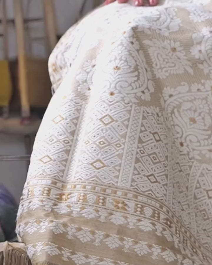 The pallu spread over the lap, moving slightly: ivory paisleys and diamond lattice on the gold ground, fingertips at the top edge.