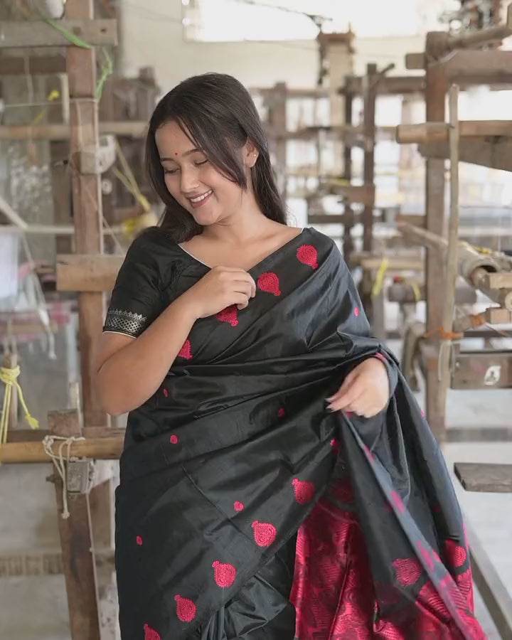 Beside a loom, lifting and spreading the pallu: red medallions on black, then the red field at its end.
